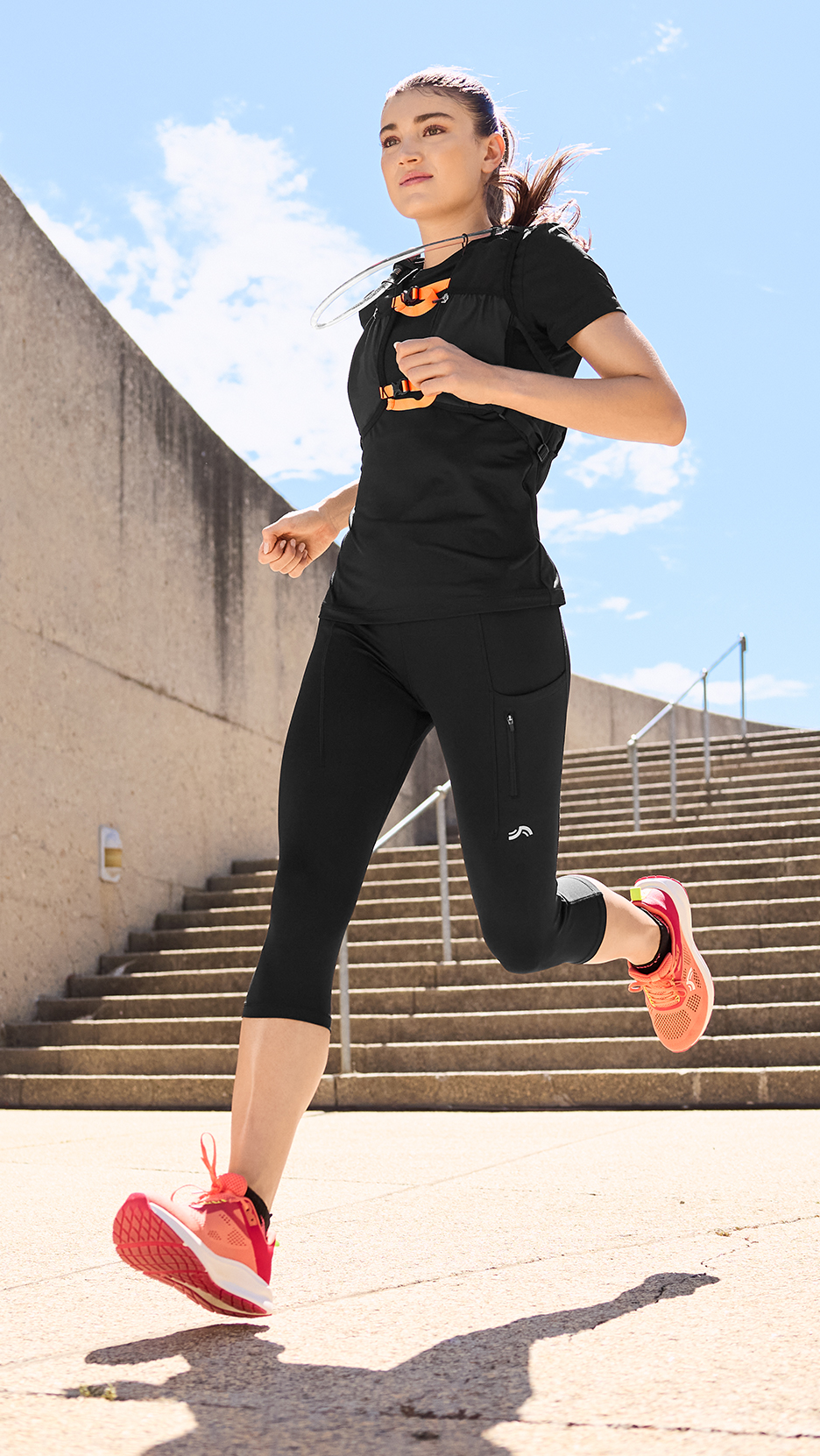 Nő futóruhában, fekete felsőben, capri nadrágban és narancssárga futócipőben.