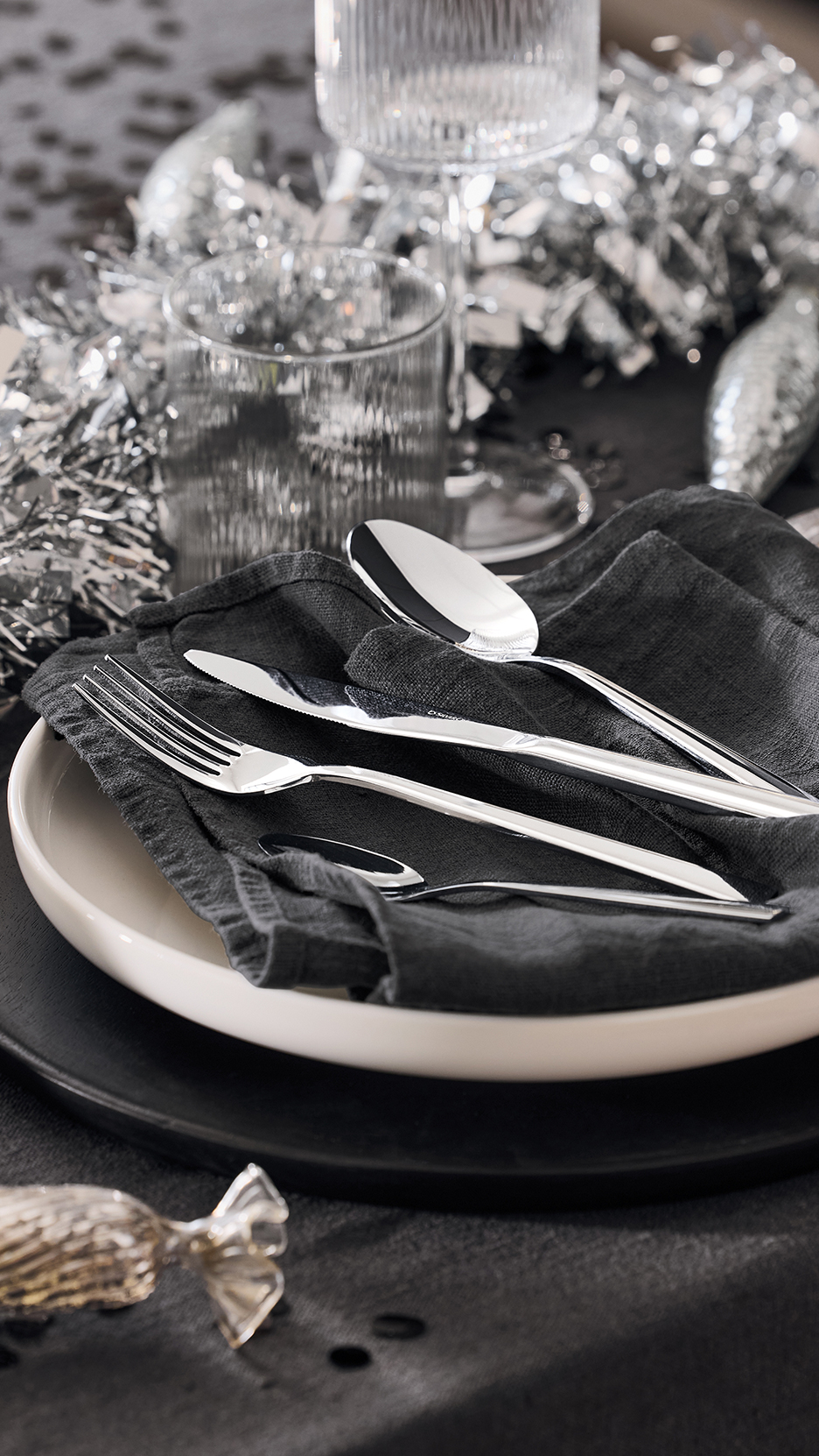Evőeszközök és tányérok ünnepi asztalon, ezüst dekorációval.