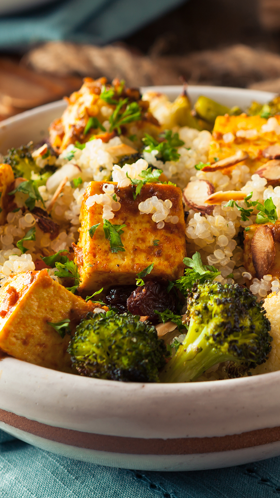 Tofu, quinoa, brokkoli és mandula egy tálban, petrezselyemmel díszítve.