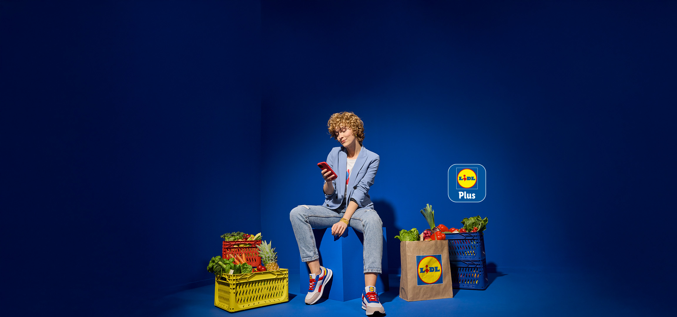 Fiatal nő telefonozik, mellette Lidl Plus logó és friss élelmiszerek.