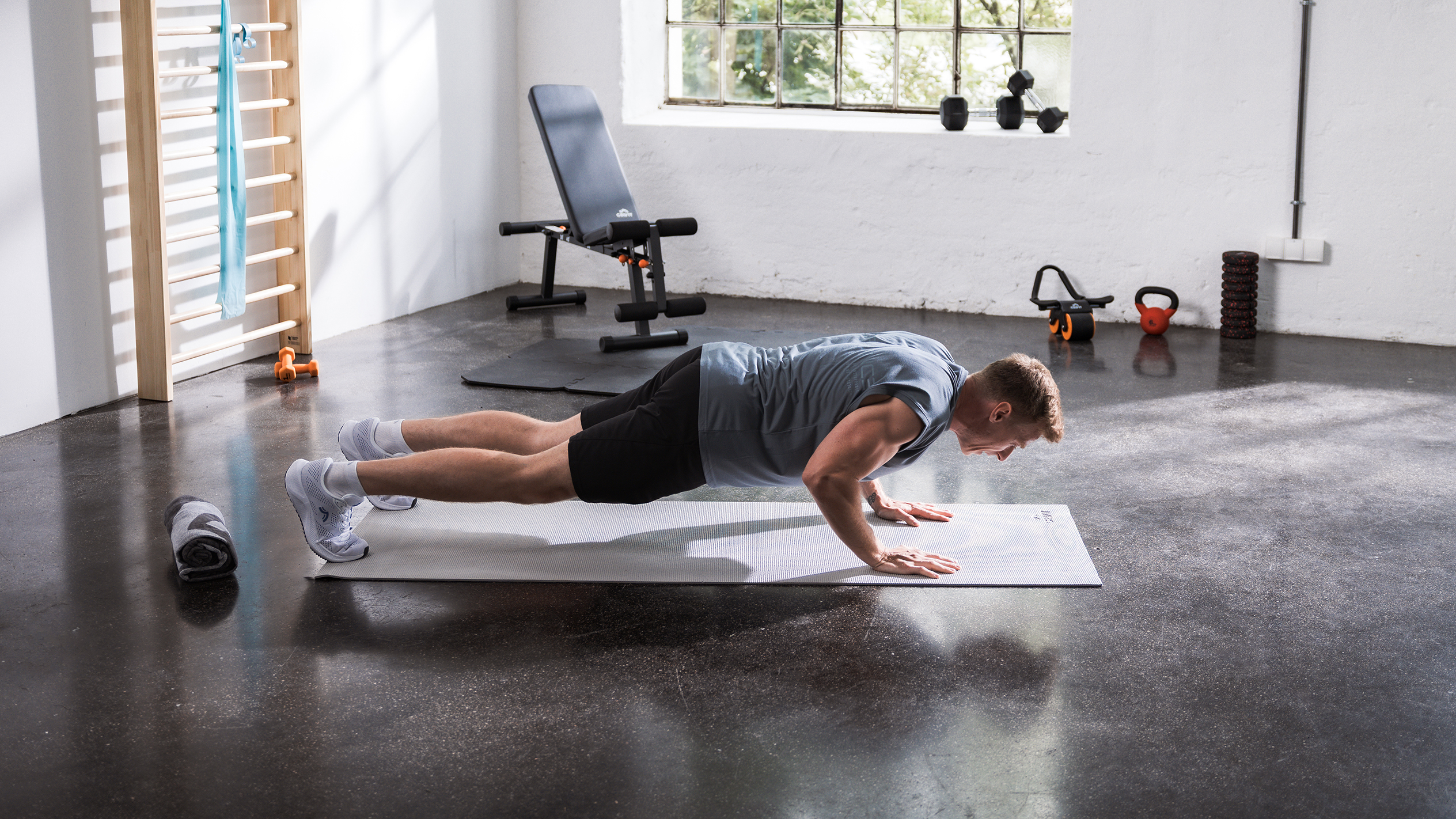 Férfi fekvőtámaszozik egy matracon otthoni edzőteremben, különféle fitneszeszközökkel.