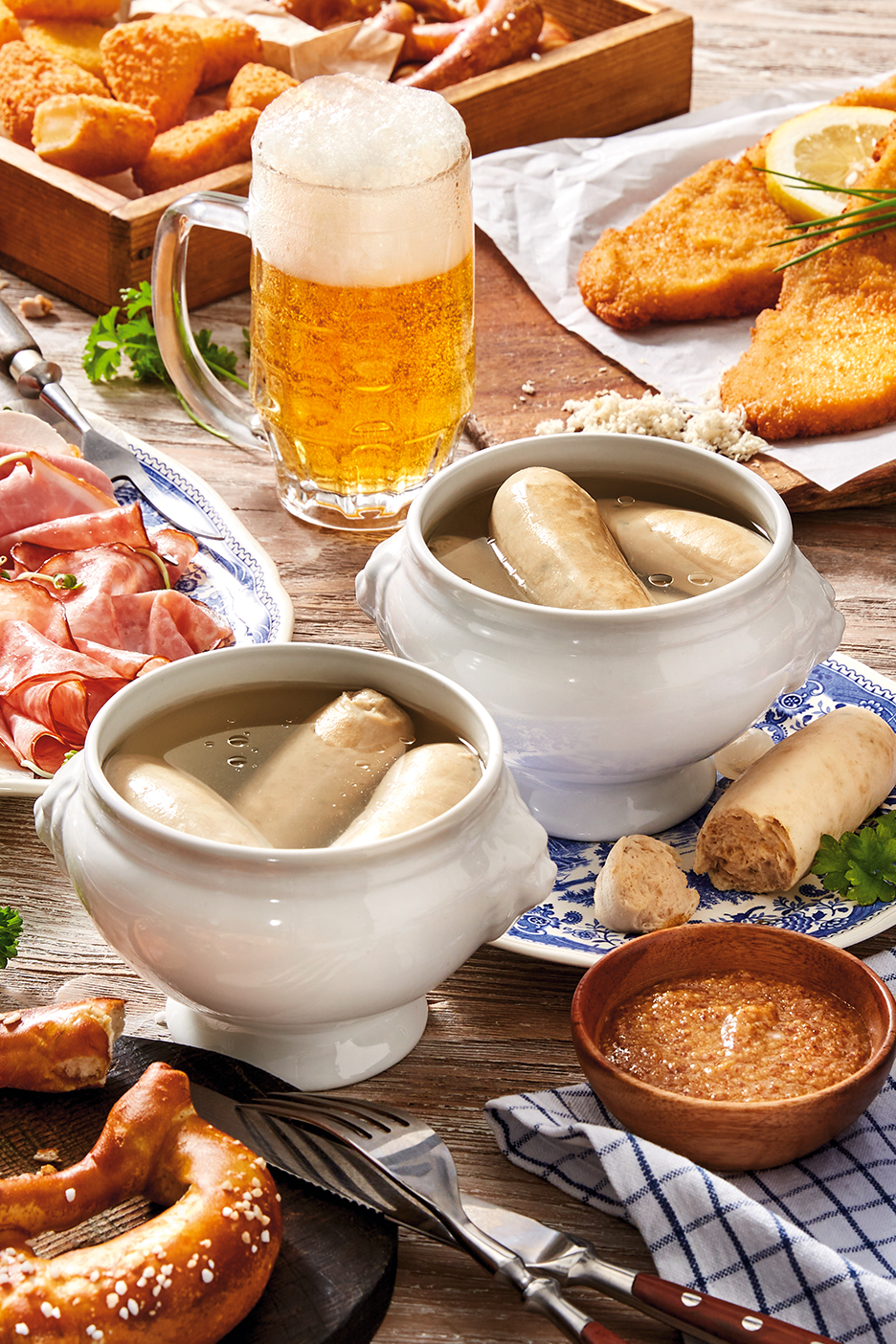 Bajor sör, fehér kolbász, perec, rántott hús és felvágottak egy asztalon.