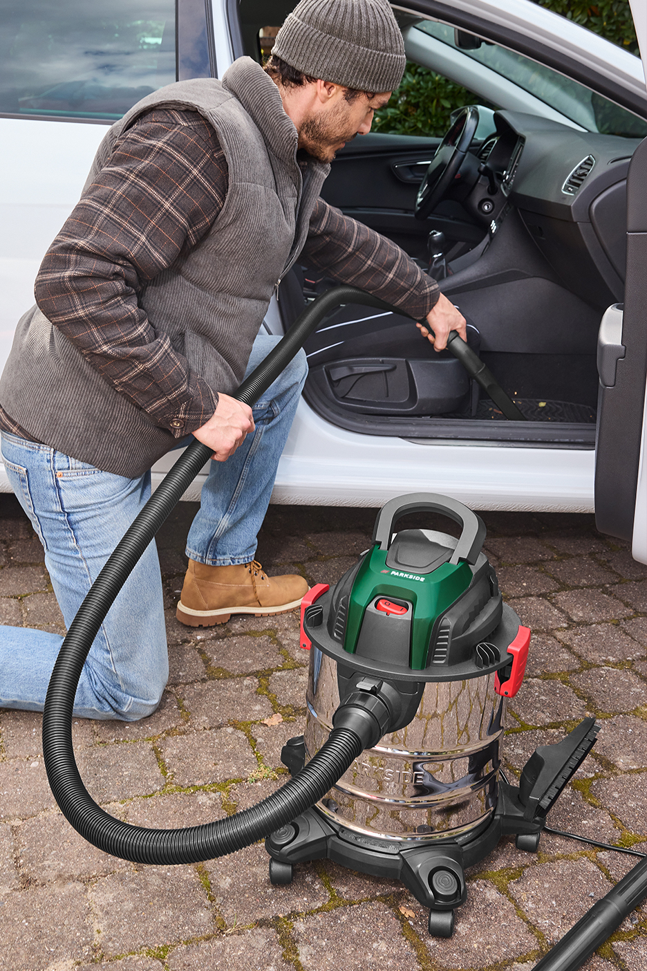 Férfi porszívóval tisztítja az autó belsejét.