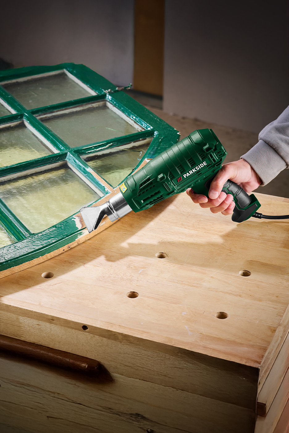 Parkside hőlégfúvóval festék eltávolítása egy zöld ablakkeretről.