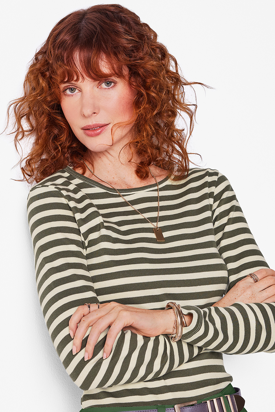 Nő zöld-bézs csíkos felsőben, arany nyaklánccal és karkötőkkel.