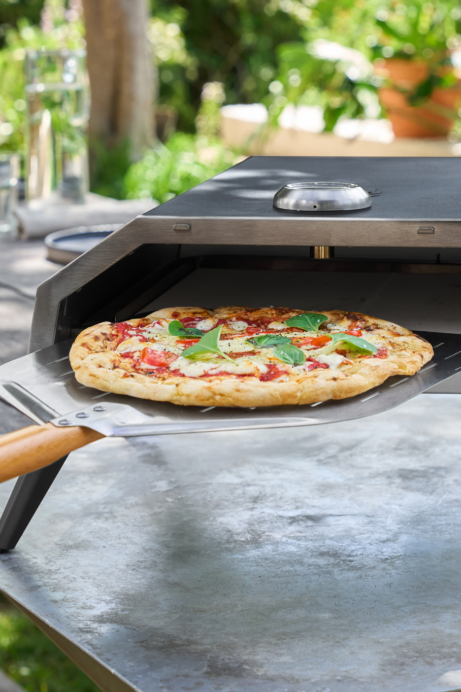 Frissen sült pizza egy kültéri pizzasütőben, pizzalapáttal.