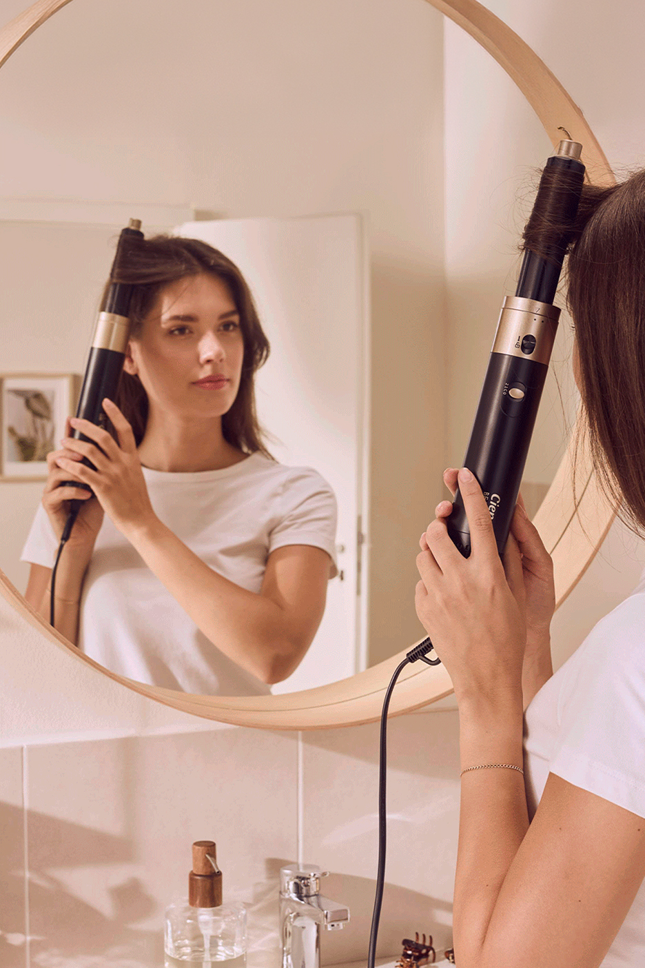 Nő tükör előtt hajszárító kefével formázza a haját.