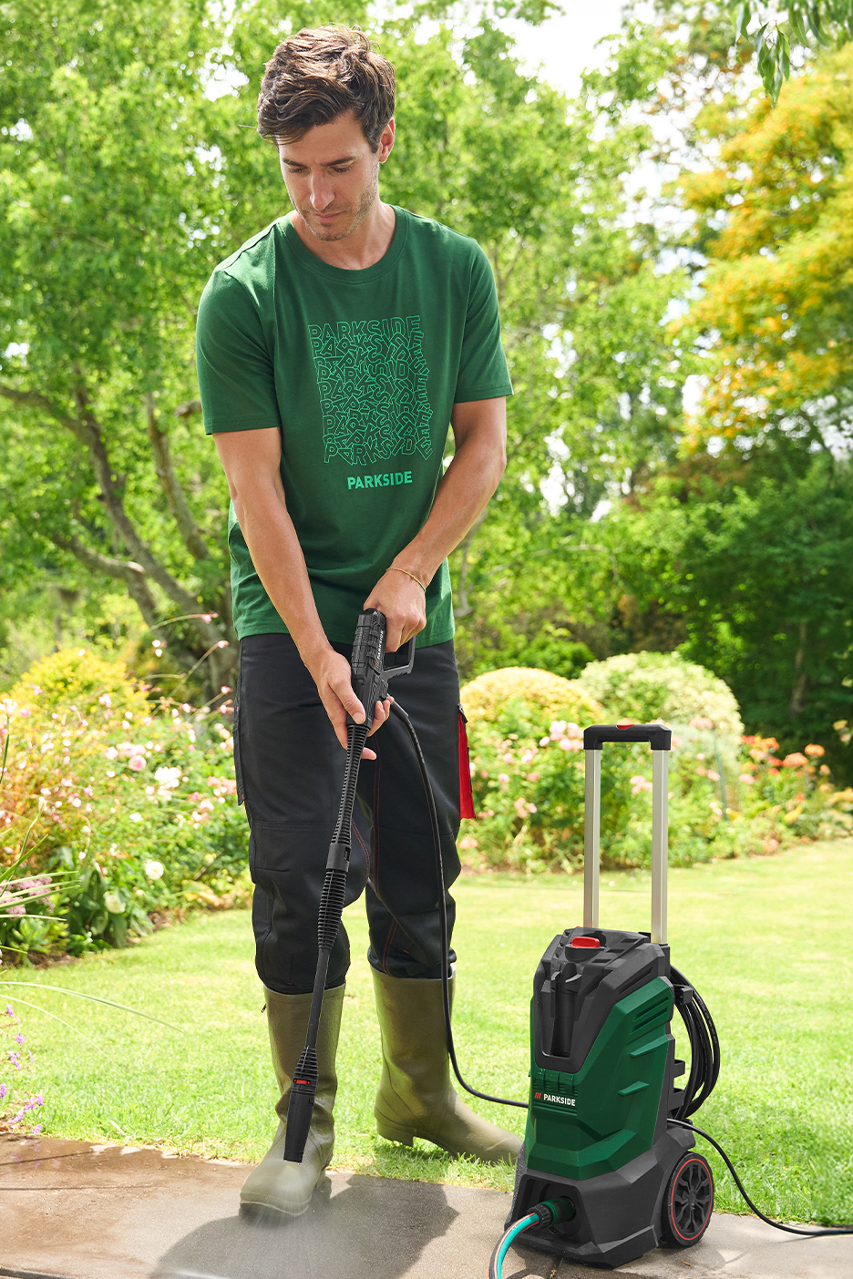 Férfi magasnyomású mosóval tisztít egy teraszt a kertben.