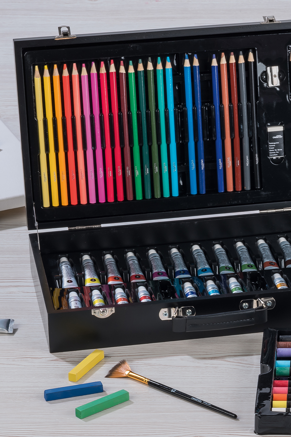Művészeti készlet nyitott fekete dobozban, színes ceruzákkal, festékekkel és pasztellkrétákkal.