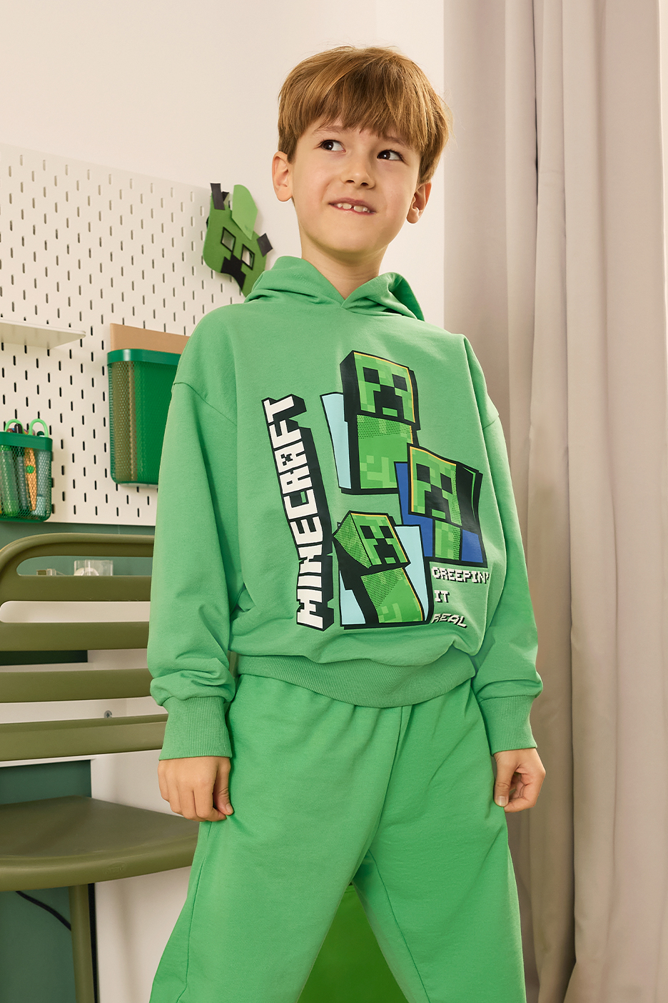 Fiú zöld kapucnis pulóverben és melegítőnadrágban, kockás mintával és felirattal.