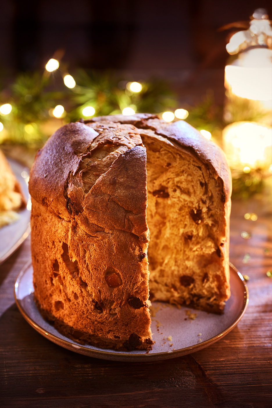 Panettone karácsonyi fényekkel és gyertyákkal egy sötét faasztalon.