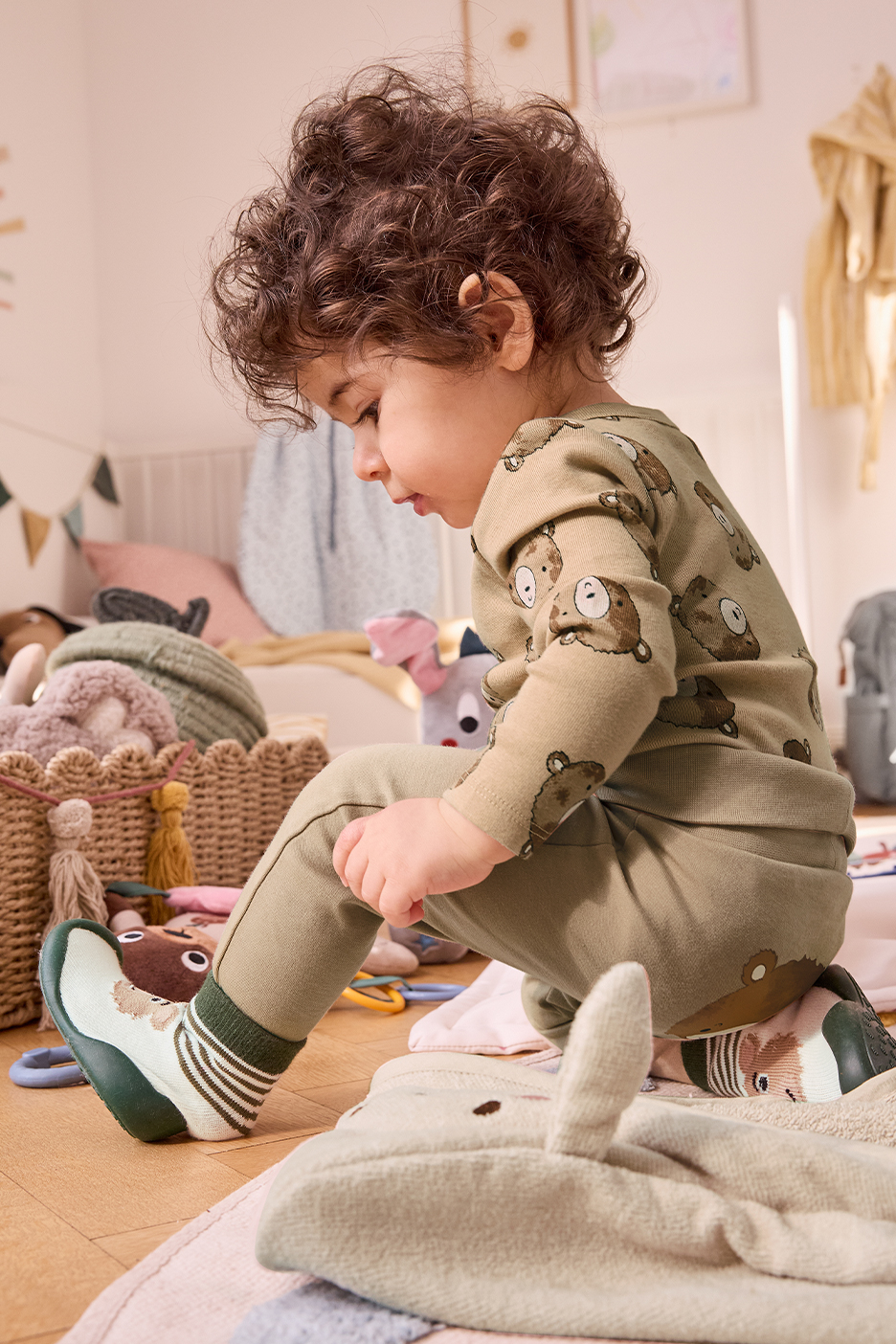 Kisfiú játszik a szobájában, zöld, medvemintás pizsamában és zoknicipőben.