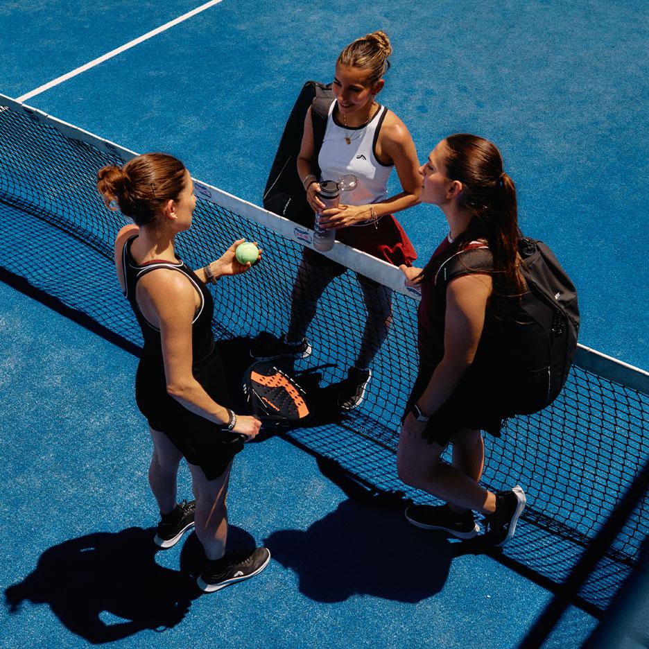 Agostina Bigotti és két csapattársa CRIVIT sportruházatban állnak a meccs után a padelhálónál egy kék pályán.
