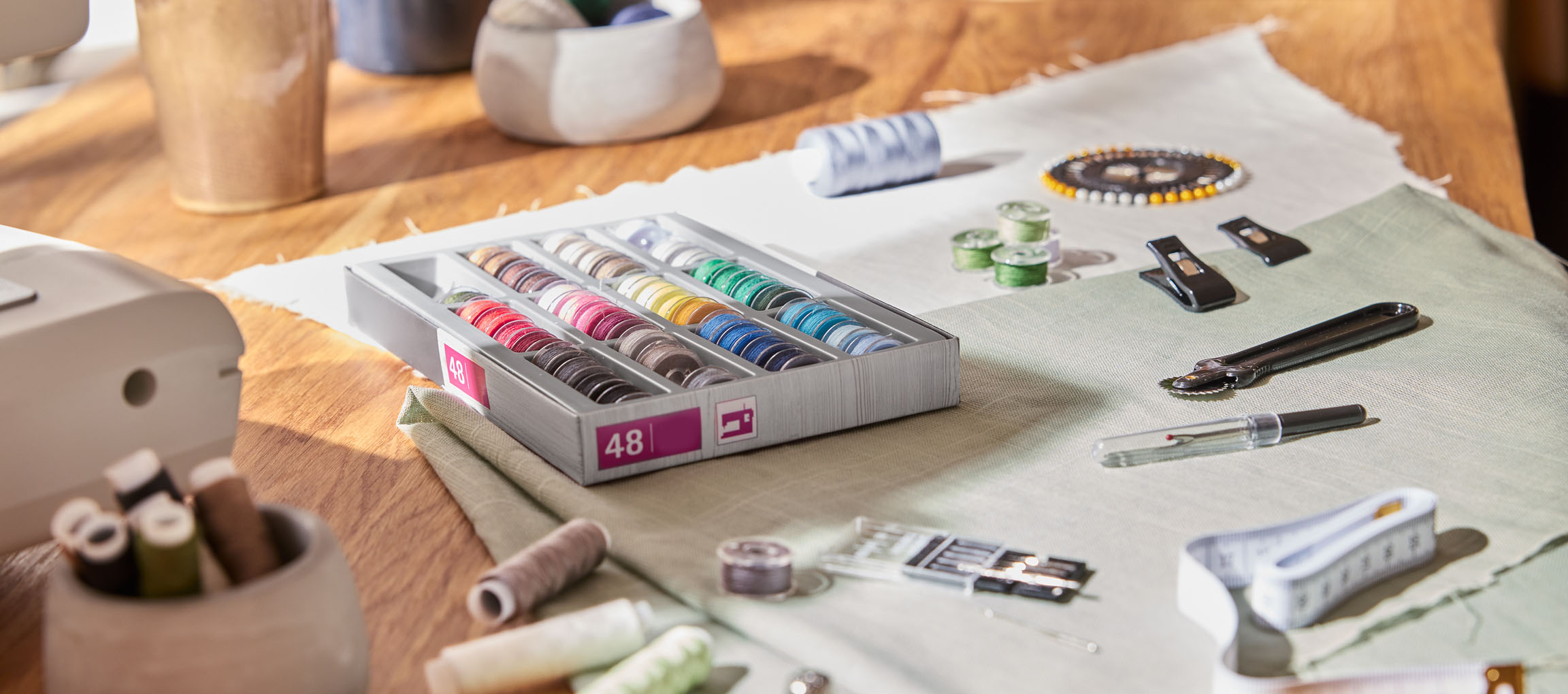 Varrókellékek fa asztalon, köztük egy 48 orsós cérnatartó, anyag és különféle eszközök.