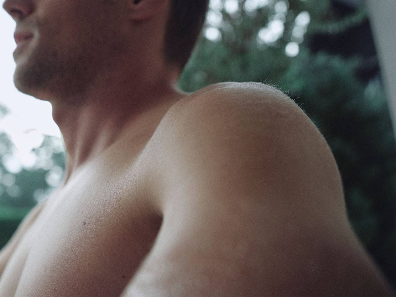 Férfi válla és nyaka közelről, elmosódott zöld háttérrel.