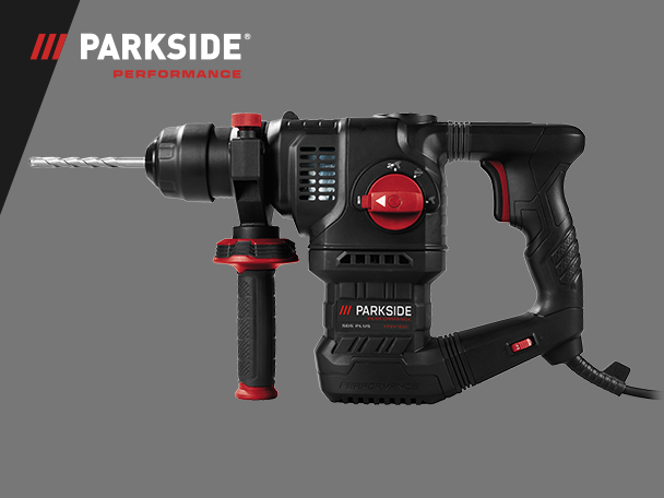 Fekete és piros fúrókalapács fúrófejjel és kiegészítő fogantyúval, szürke háttér előtt.