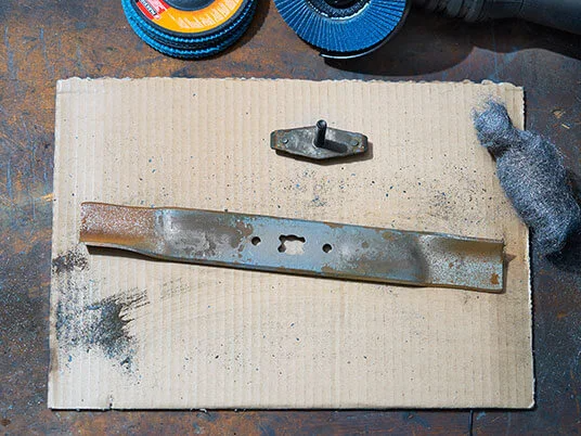 Rozsdás fűnyírópenge kartonon csiszolókorongokkal és acélgyapottal.