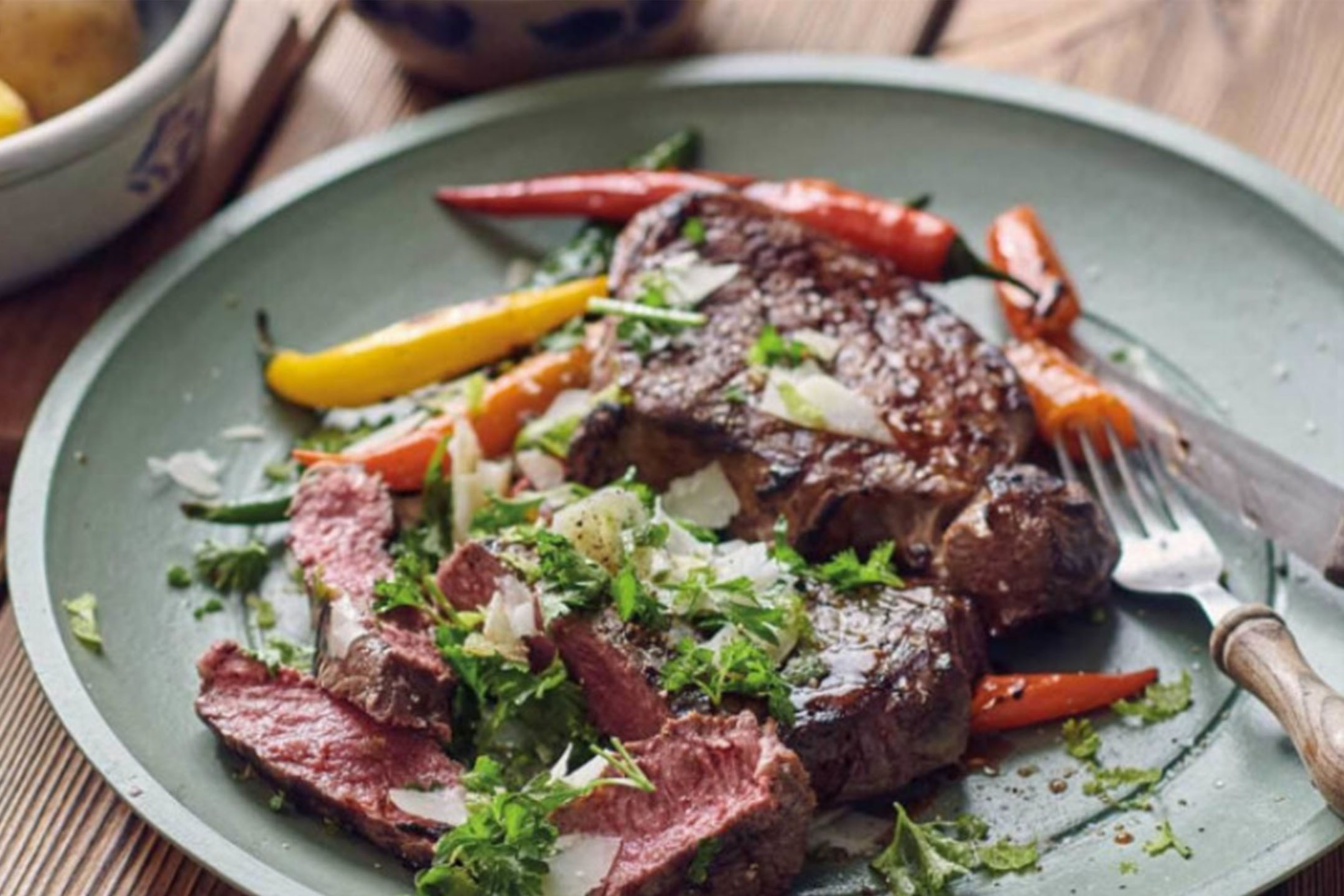 Grillezett steak paprikával, friss fűszernövényekkel és reszelt sajttal zöld tányéron.