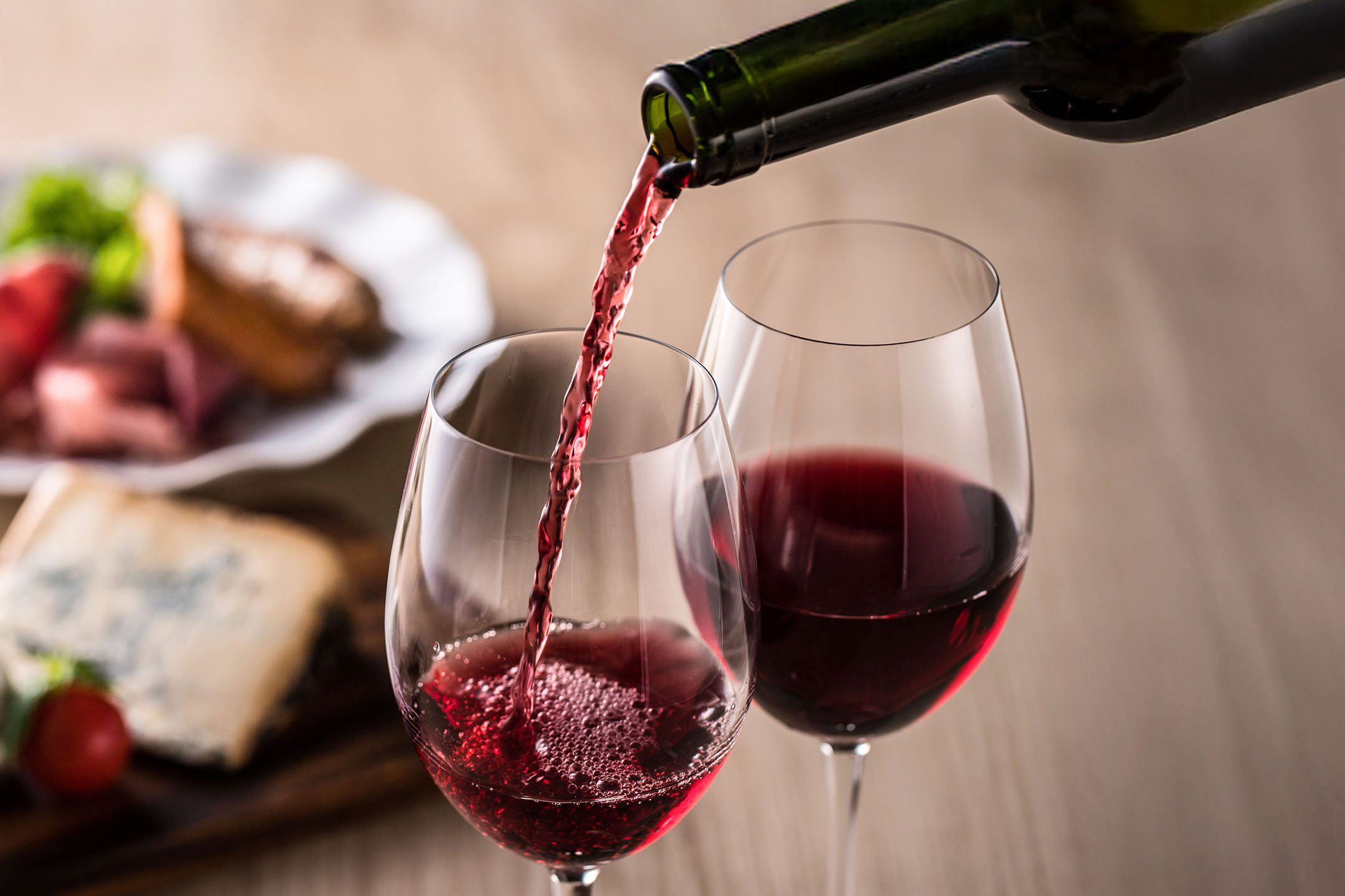 Vörösbor öntése pohárba, előételekkel a háttérben.