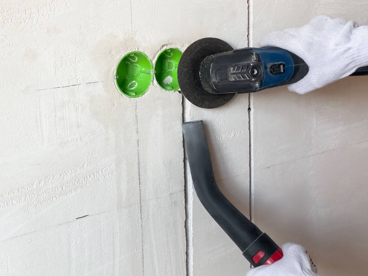 Elektromos szerszám vág barázdákat a falba porszívóval a porhoz.