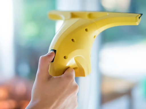 Kéz tart egy sárga elektromos ablaktisztítót, ablakot tisztítva.