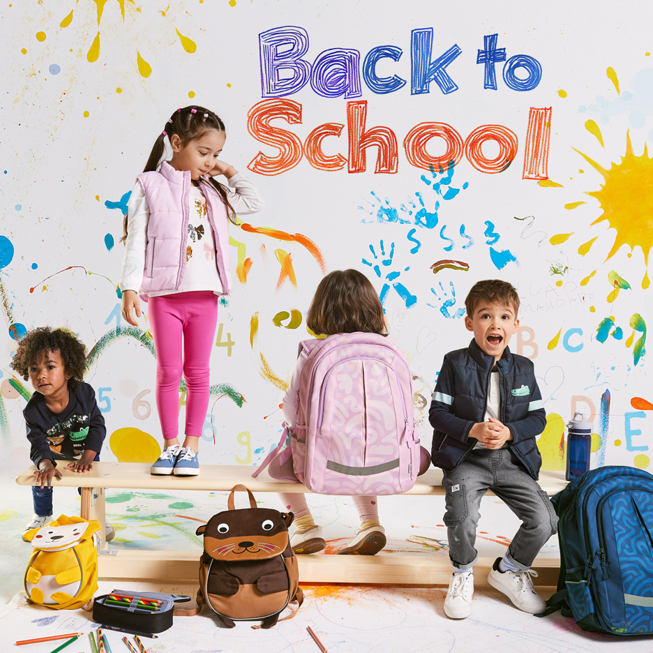 Négy gyermek hátizsákkal és iskolaszerekkel, „Back to School” felirattal színes háttéren.