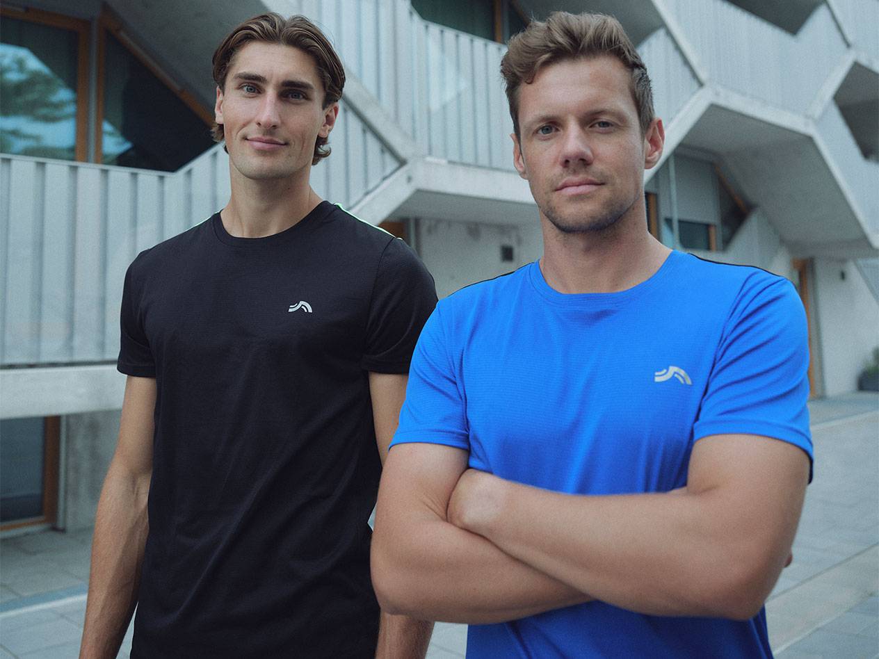 Két férfi fekete és kék sportpólóban, logóval.