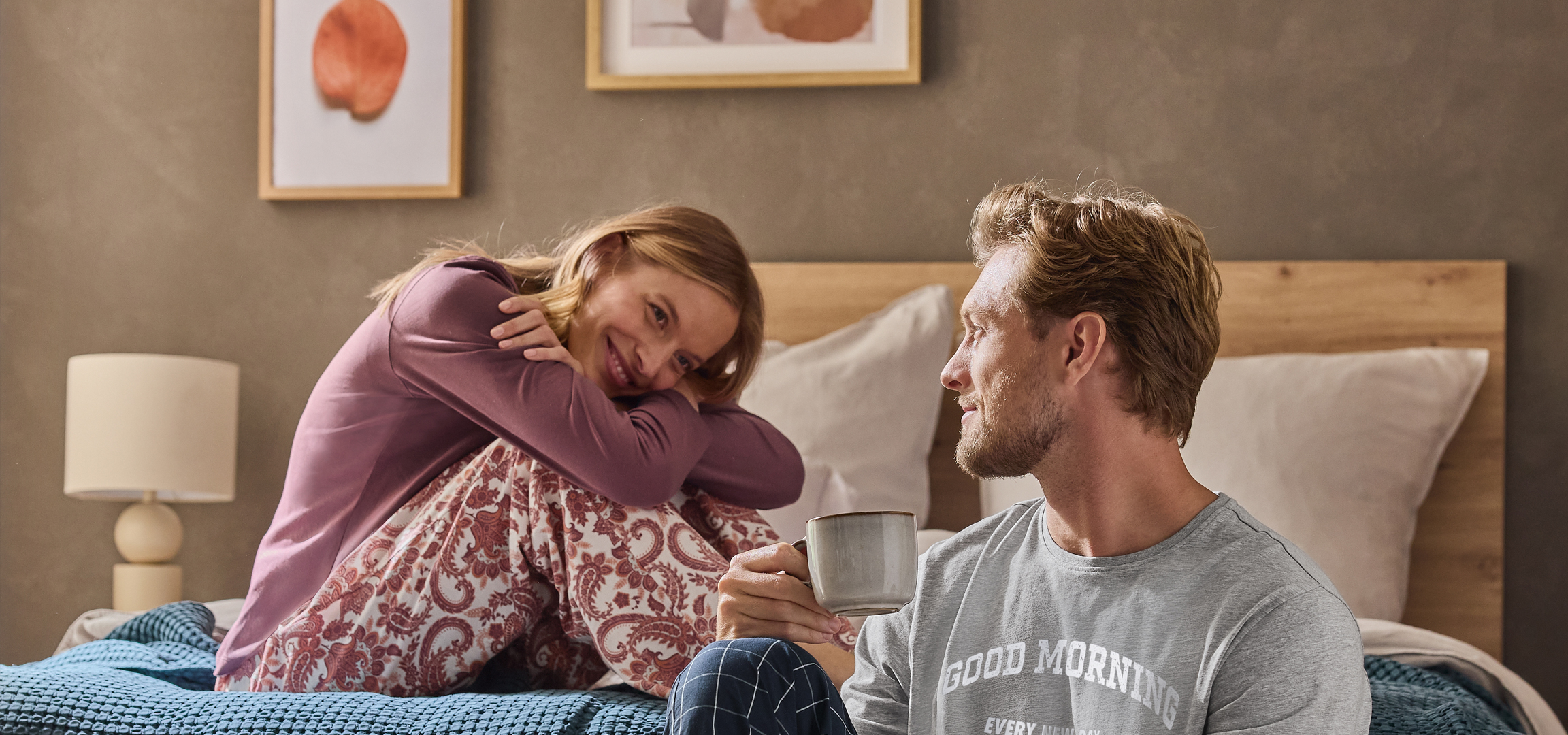 Pizsamás pár kávézik az ágyban, a nő virágmintás nadrágot visel.