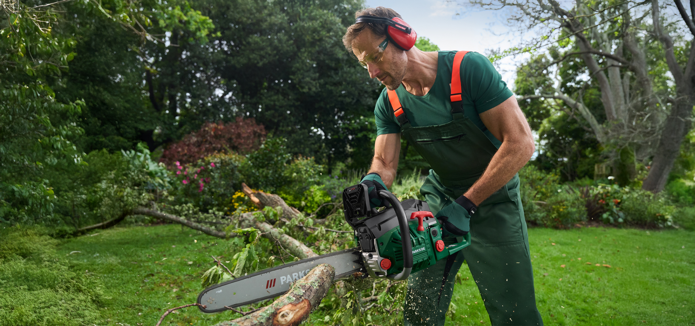 Férfi láncfűrésszel vágja a fát a kertben, védőfelszerelésben.