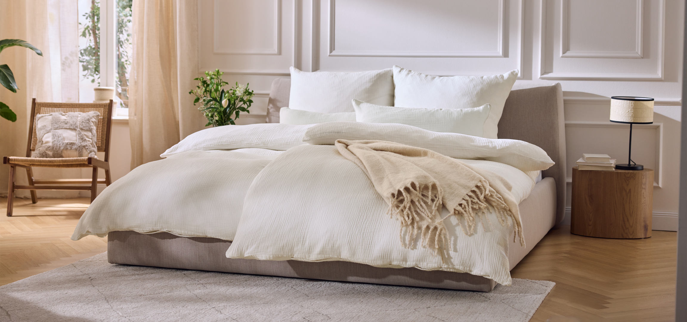 Hálószoba világos ágyneművel, növényekkel és fa bútorokkal.