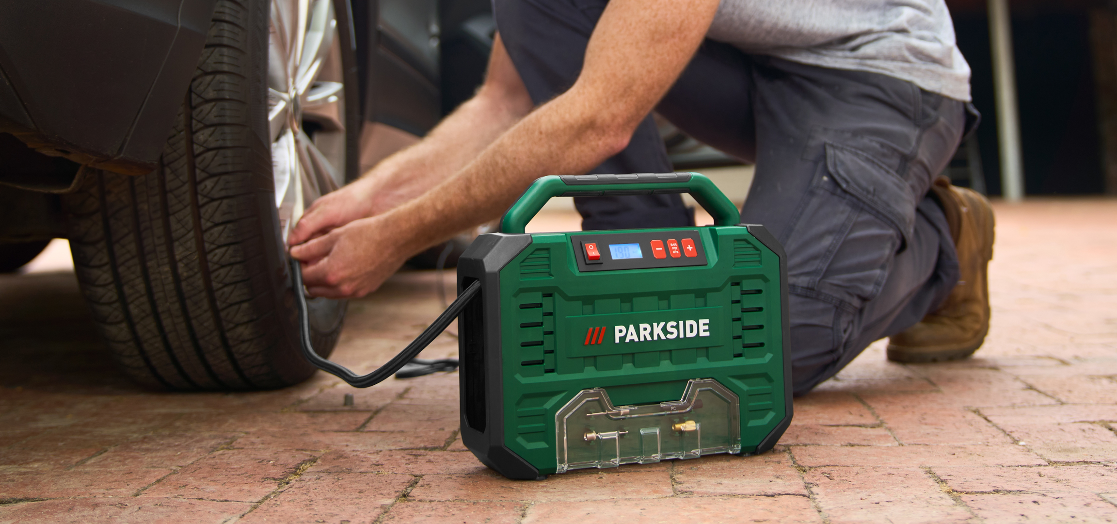 Férfi pumpálja az autó kerekét egy hordozható kompresszorral.