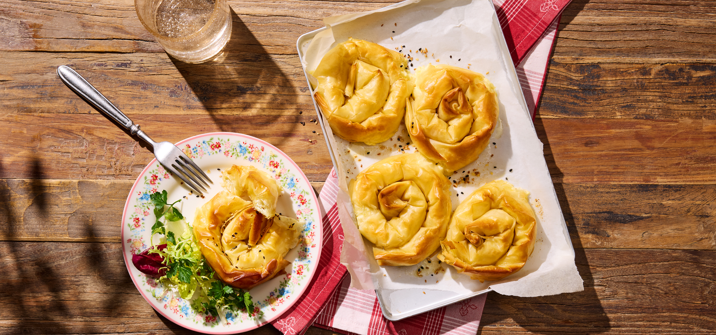 Sajtos tekercsek salátával és egy pohár vízzel egy rusztikus faasztalon.