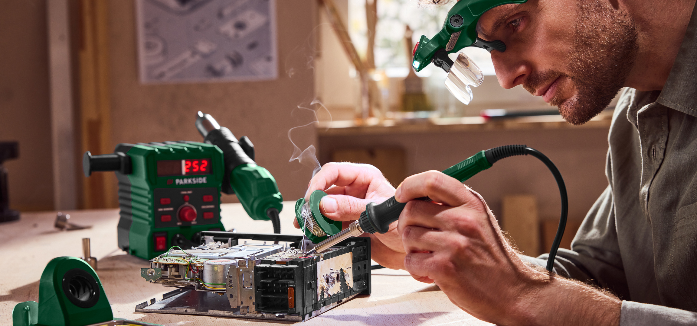 Férfi forrasztópákával és forrasztóállomással dolgozik egy elektronikai eszközön.