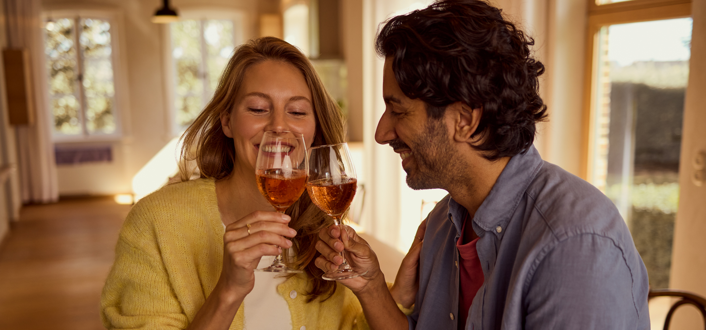 Pezsgővel koccintó pár egy otthonos nappaliban.