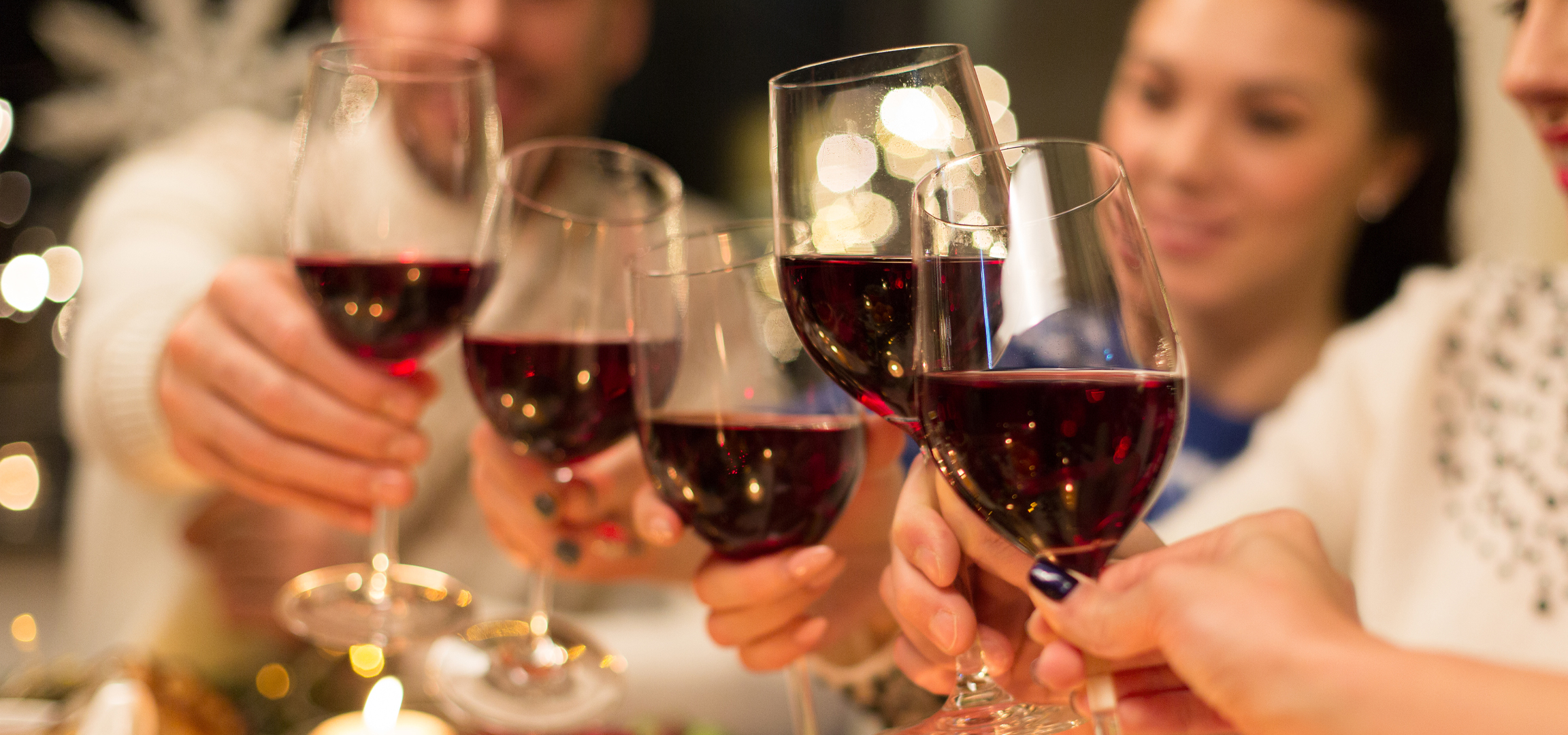 Emberek koccintanak vörösborral, ünnepi hangulatban, elmosódott fényekkel.