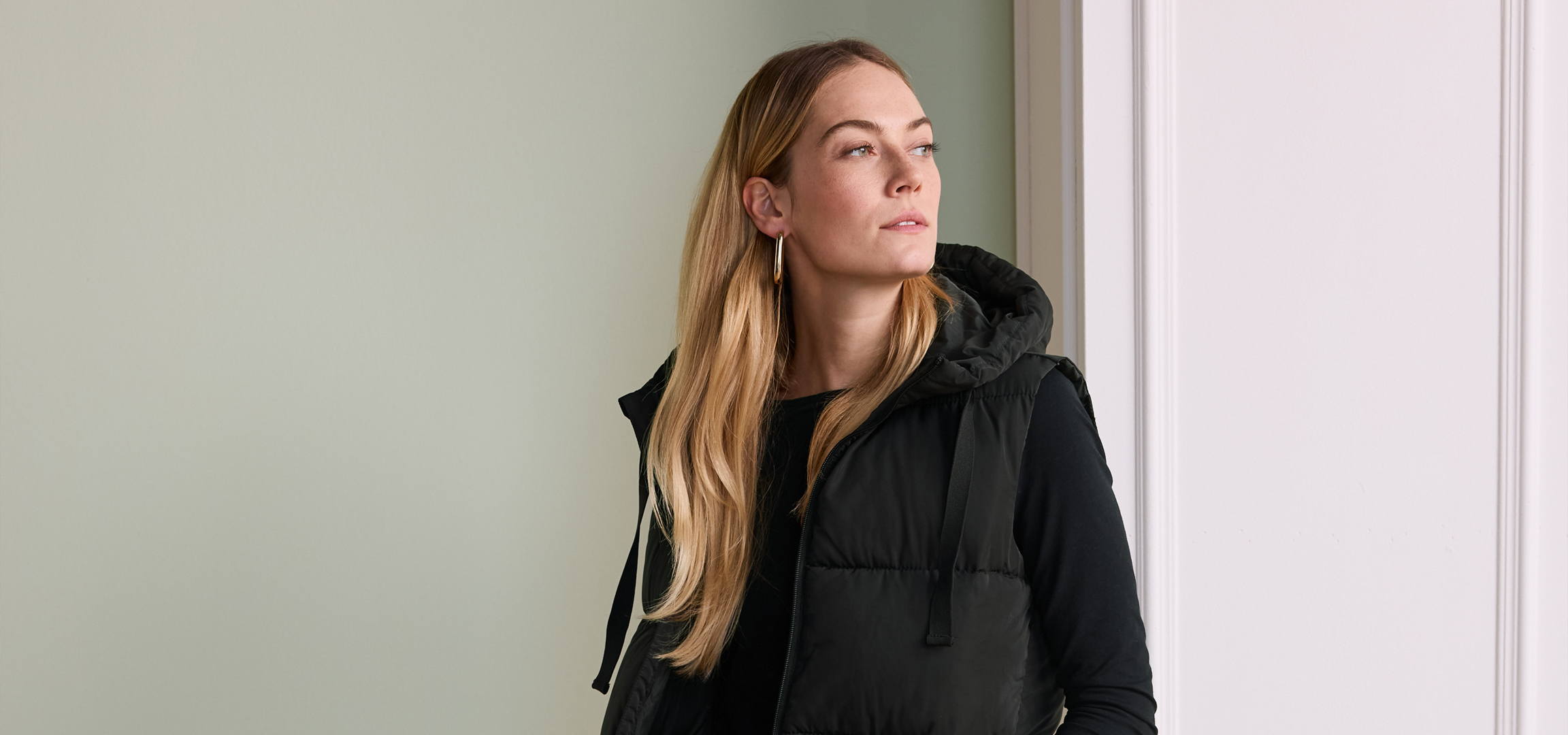 Női fekete mellény és zöld nadrág, oldalt állva.