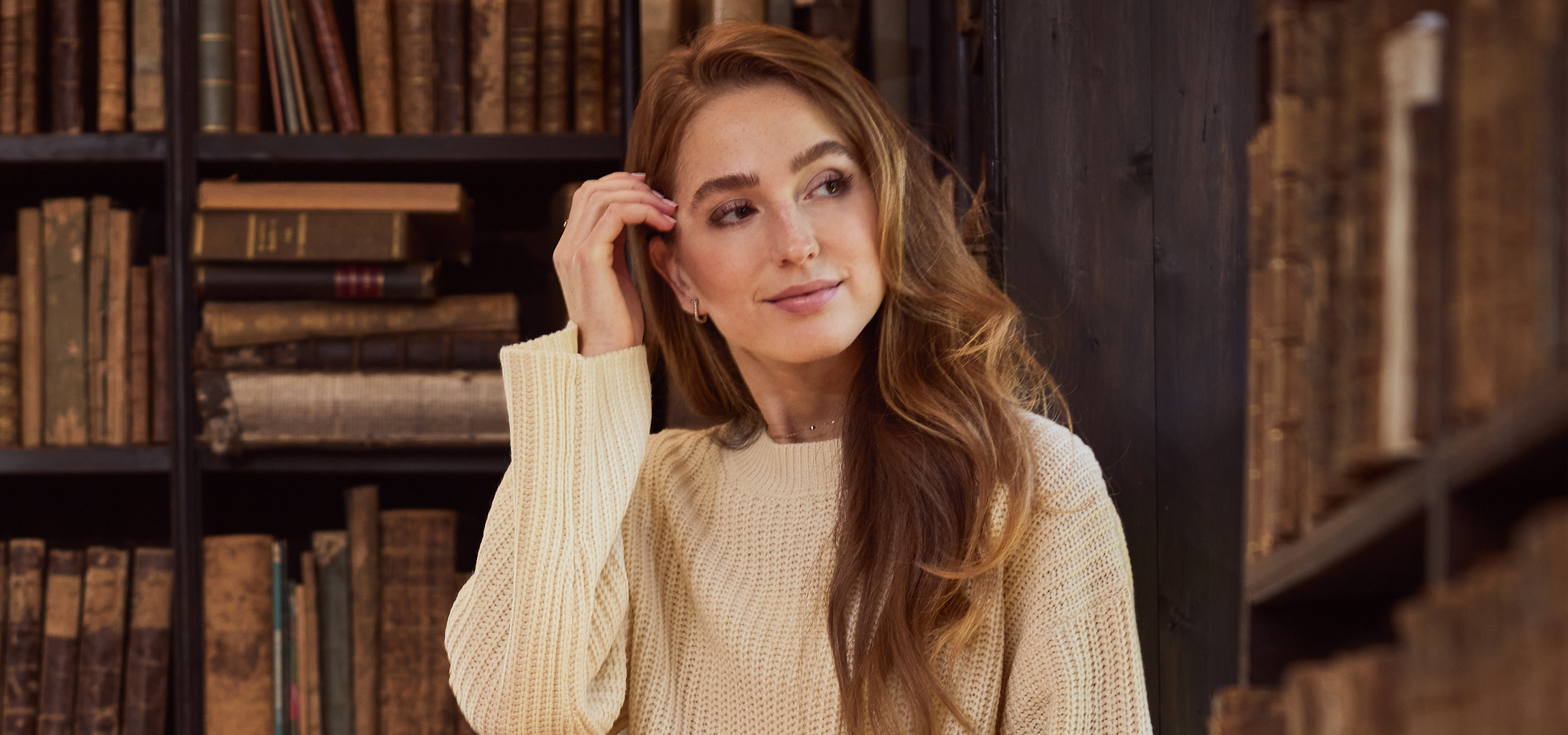 Fiatal nő egy régi könyvtárban, tele könyvespolcokkal.