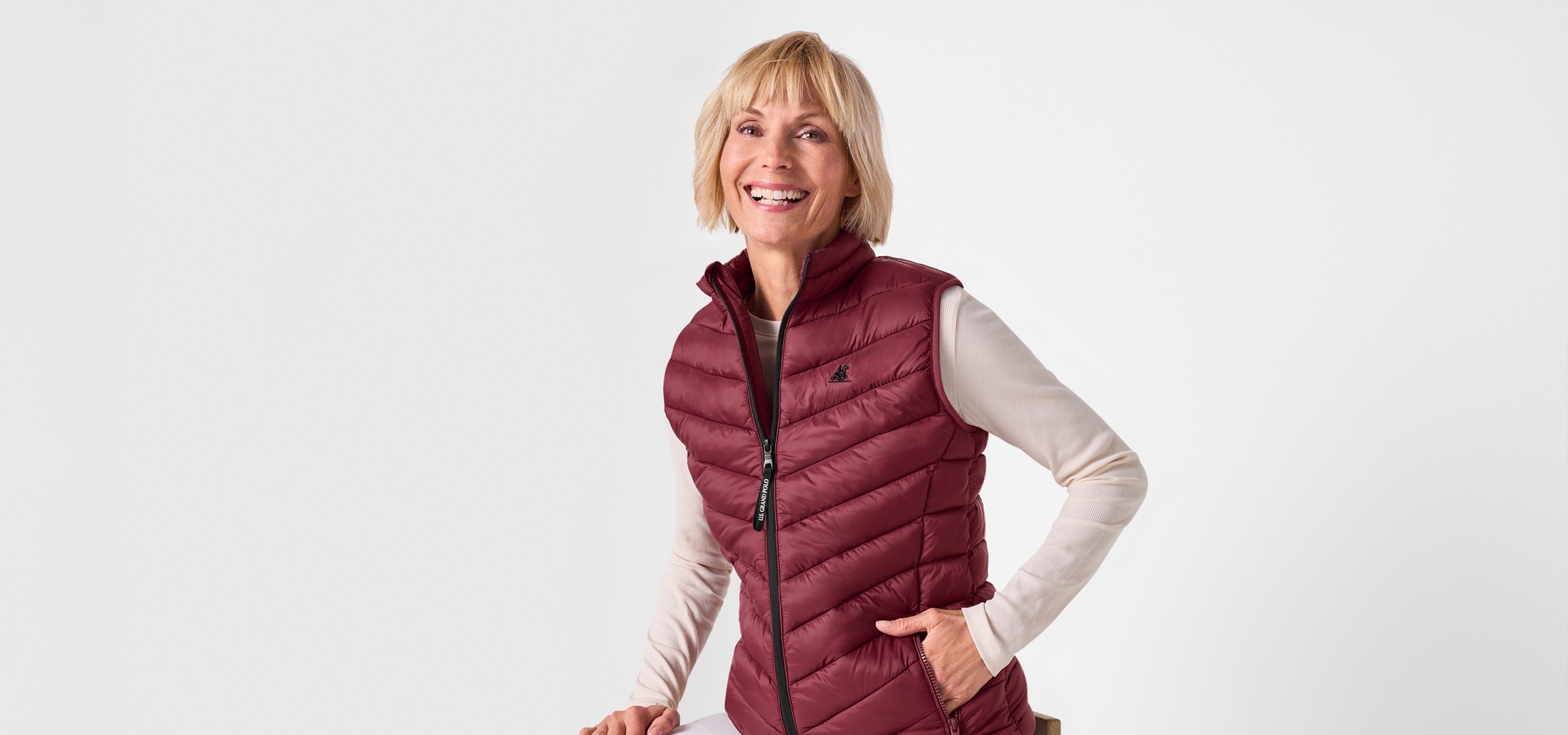 Mosolygó nő bordó mellényben és világos felsőben, fehér háttér előtt.