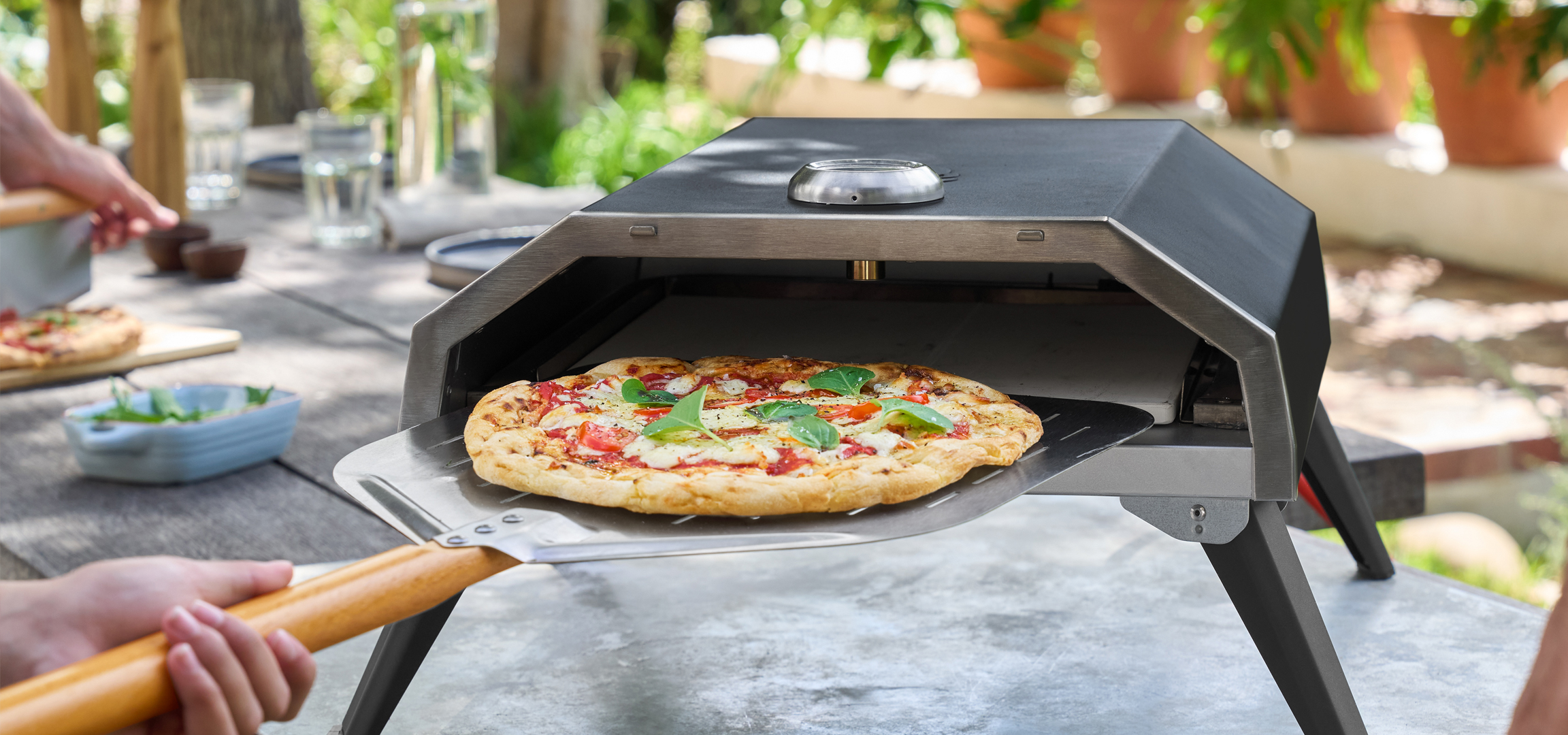 Kültéri pizzasütő frissen sült pizzával és emberekkel, akik pizzát készítenek.