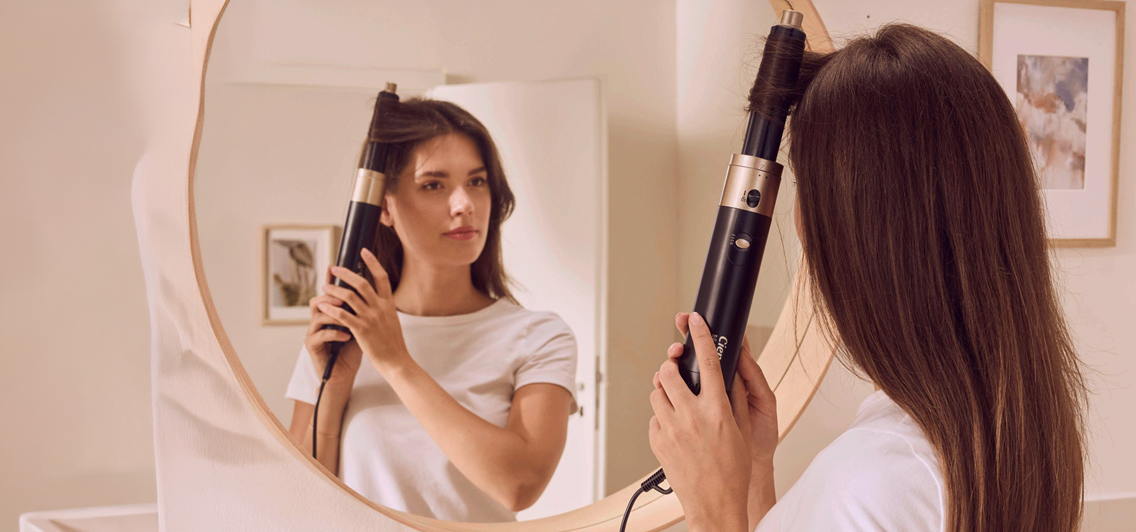 Nő tükör előtt hajszárítóval formázza a haját.