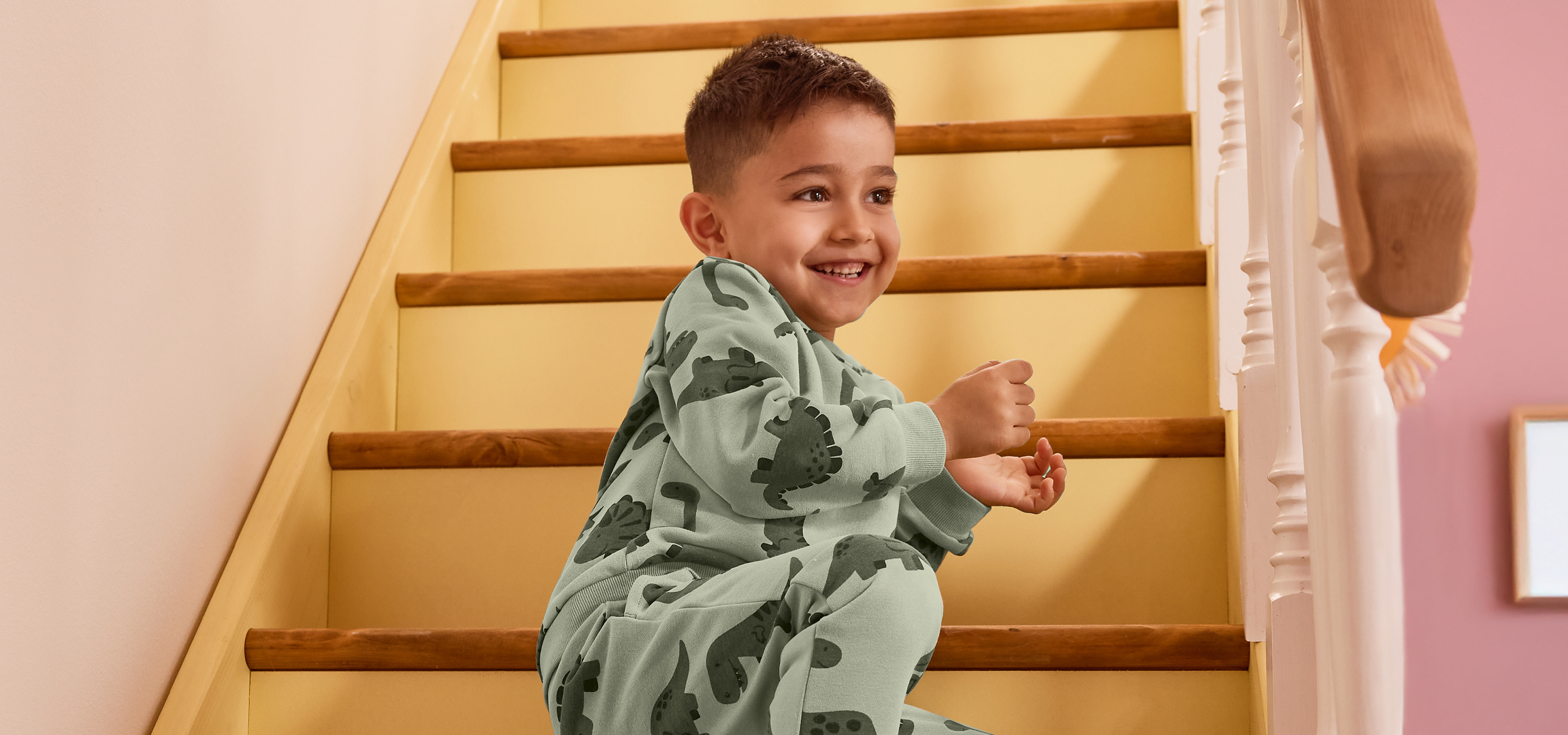Mosolygós kisfiú dinoszauruszos pizsamában, felfelé szalad a lépcsőn.