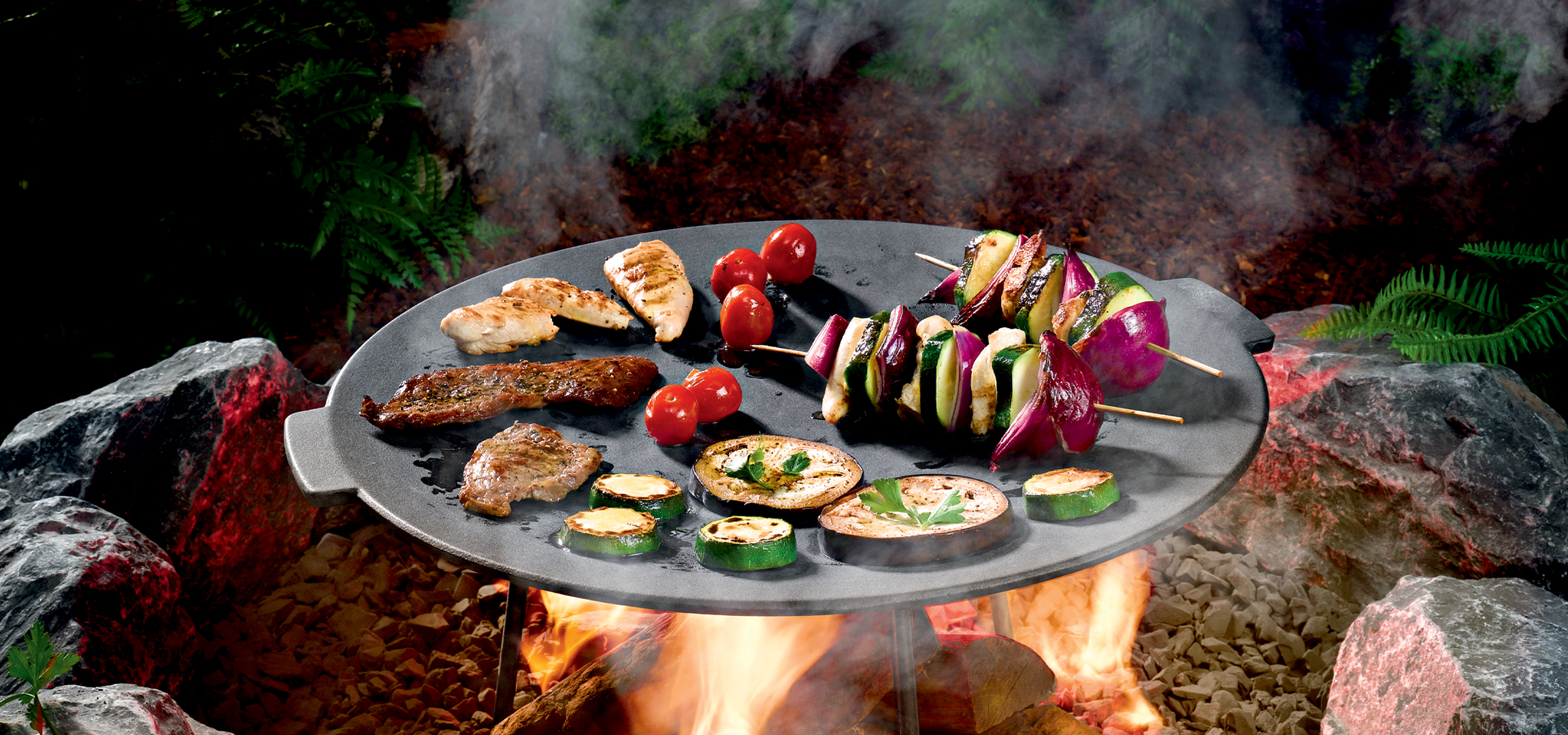 Grillezett húsok és zöldségek egy kerek grilltálon, tábortűz felett.