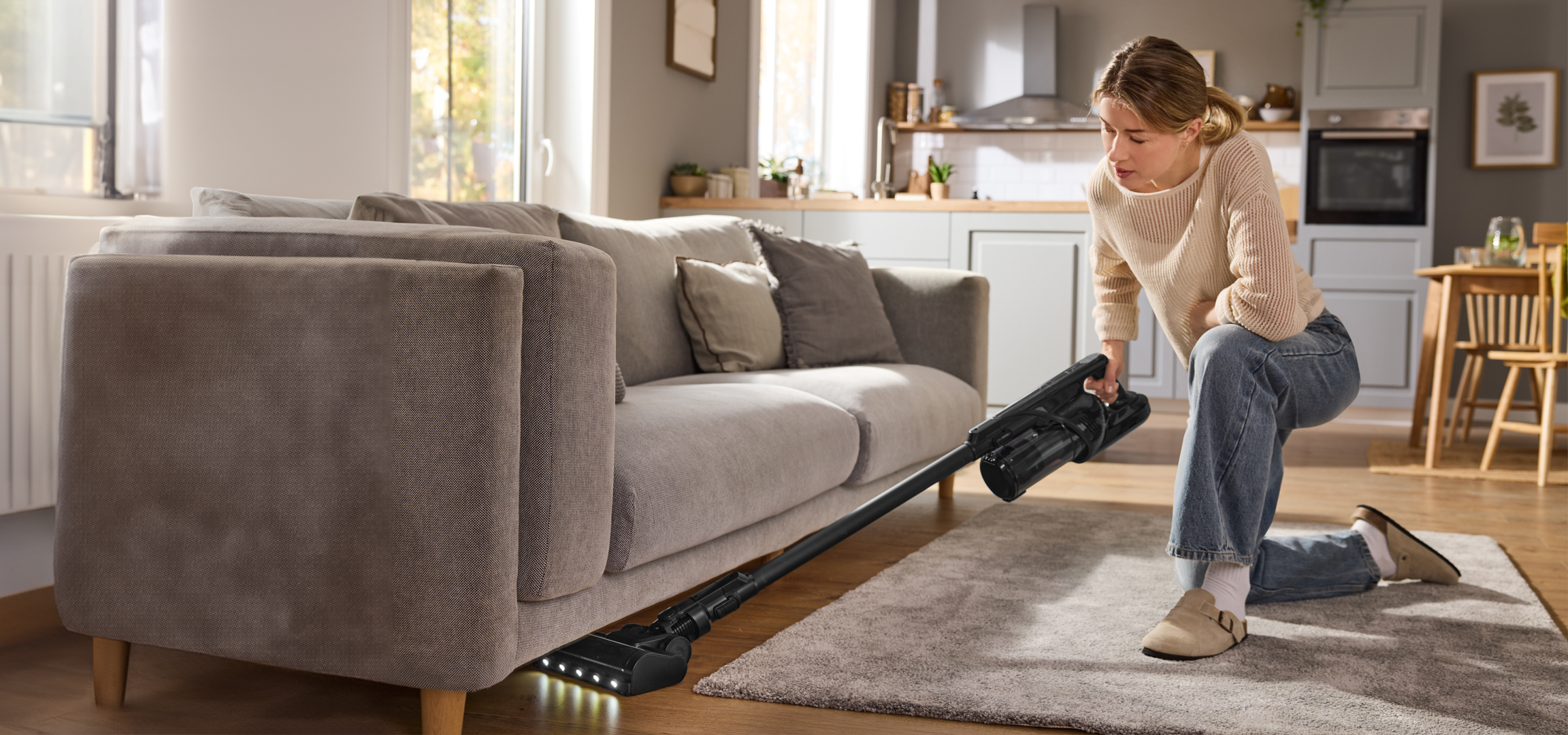Nő porszívózik a kanapé alatt a nappaliban.