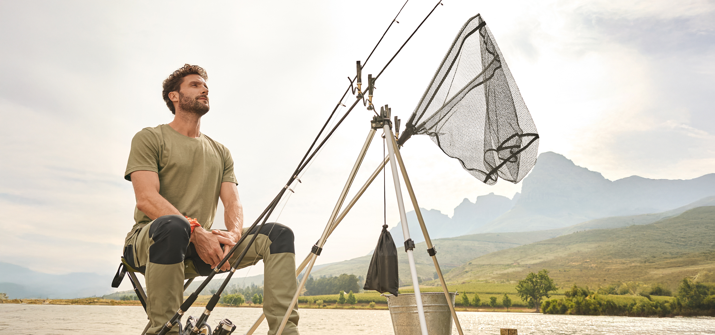 Férfi horgászik egy tavon horgászbotokkal, merítőhálóval és vödörrel.