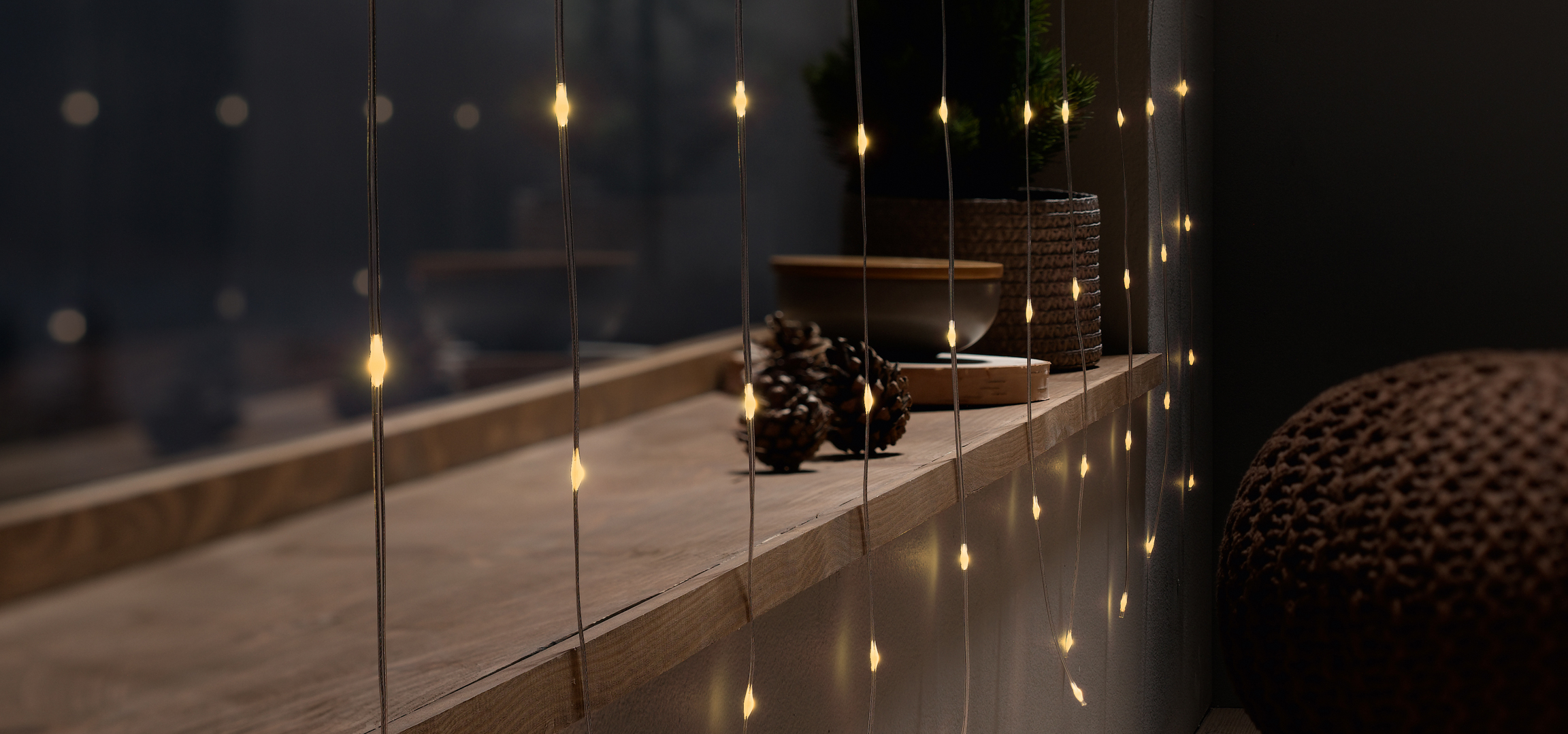 Karácsonyi fényfüzér fenyőtobozokkal és dekorációval egy polcon.