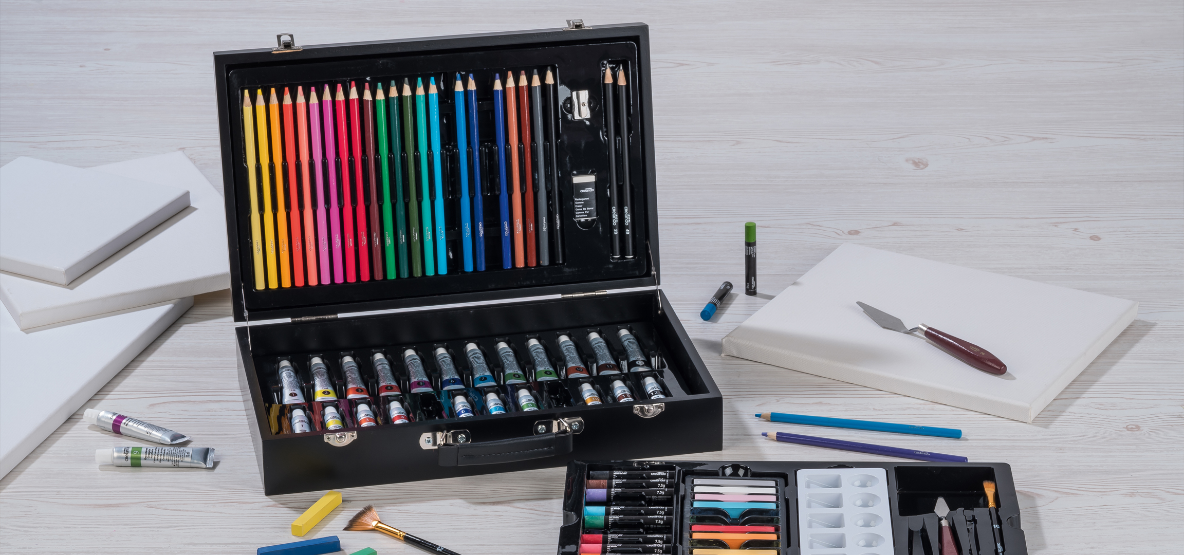 Művészeti készlet színes ceruzákkal, festékekkel és vászonnal egy világos fa felületen.
