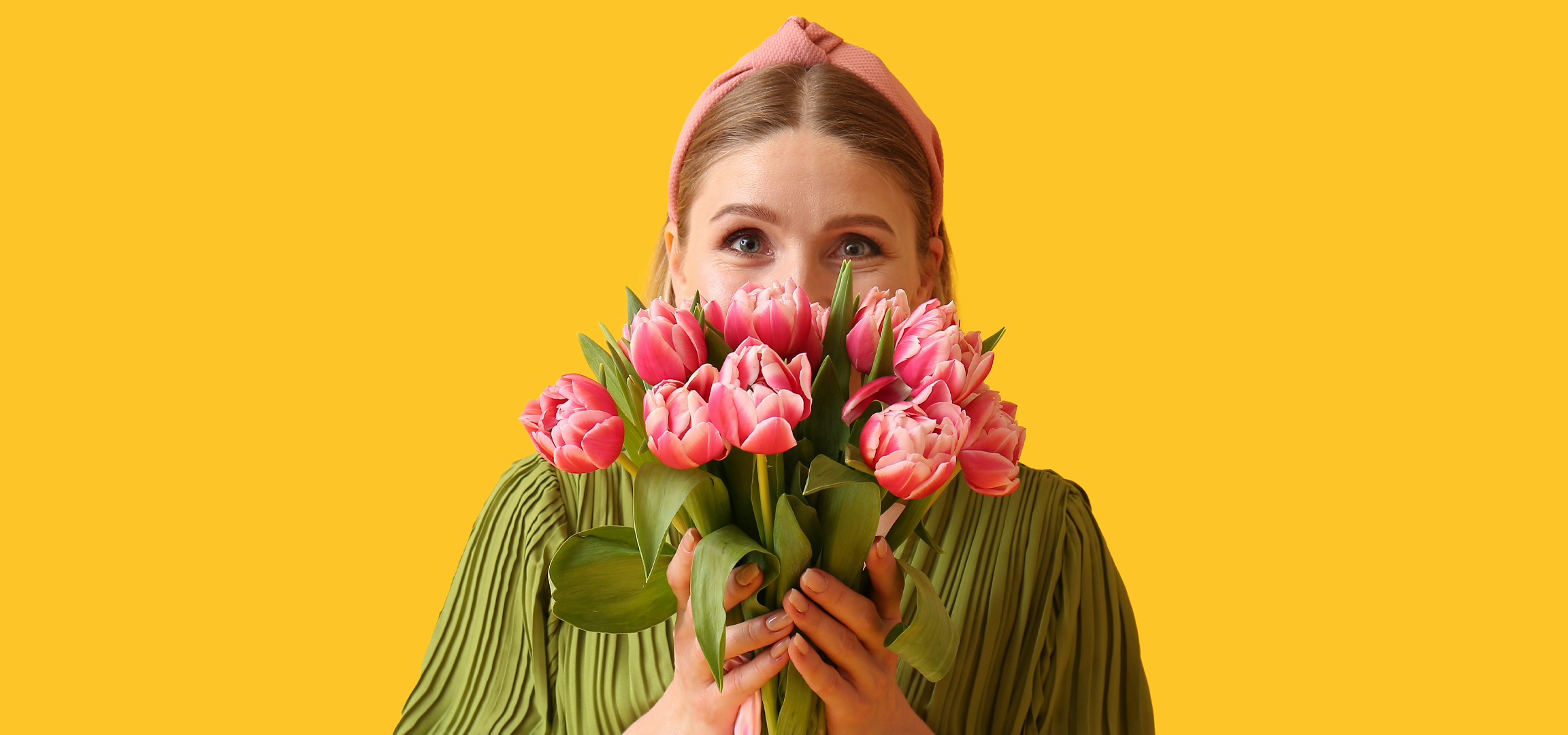 Nő rózsaszín tulipáncsokorral, sárga háttér előtt.