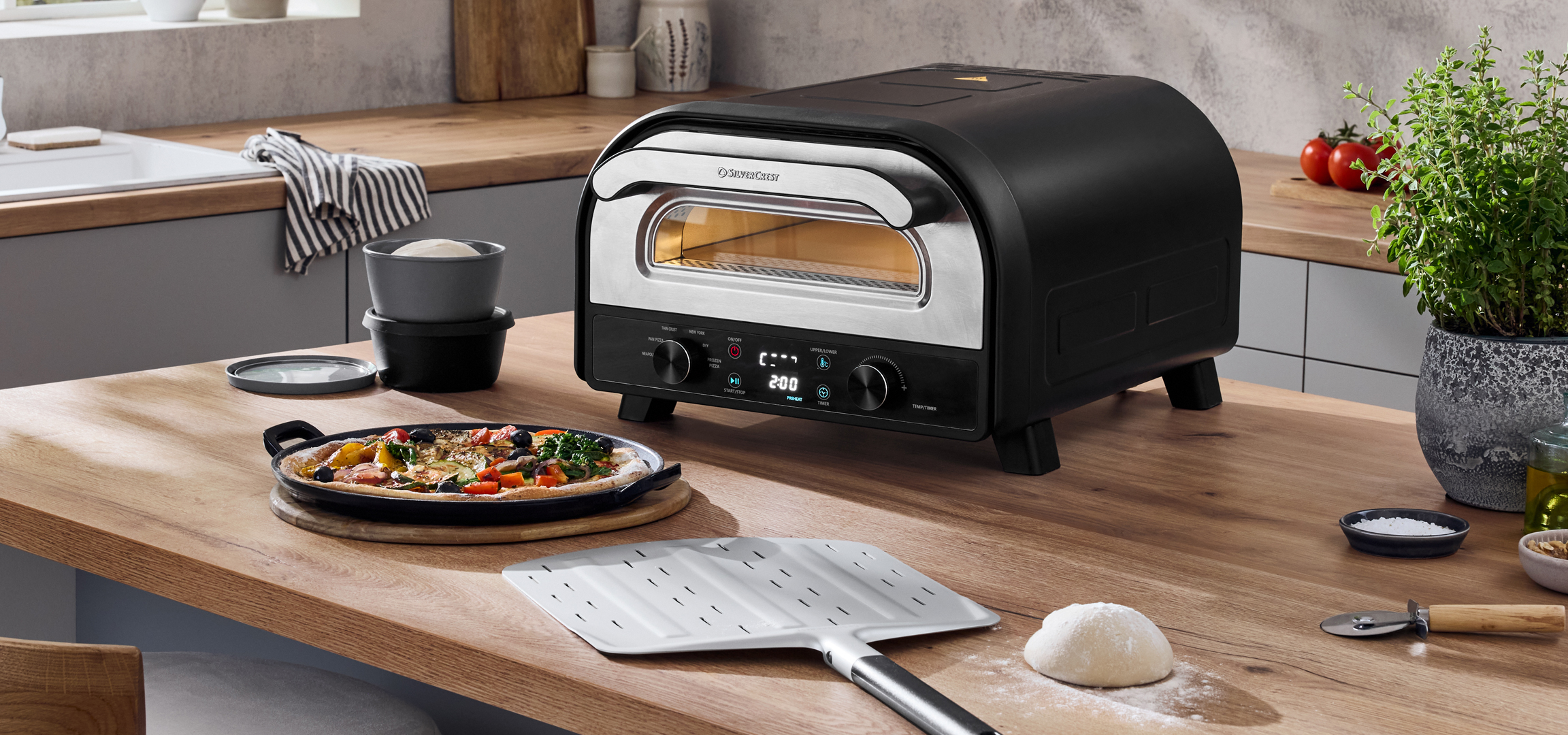 Konyha pizzakemencével, pizzával, pizzalapáttal és tésztával egy fa konyhaszigeten.