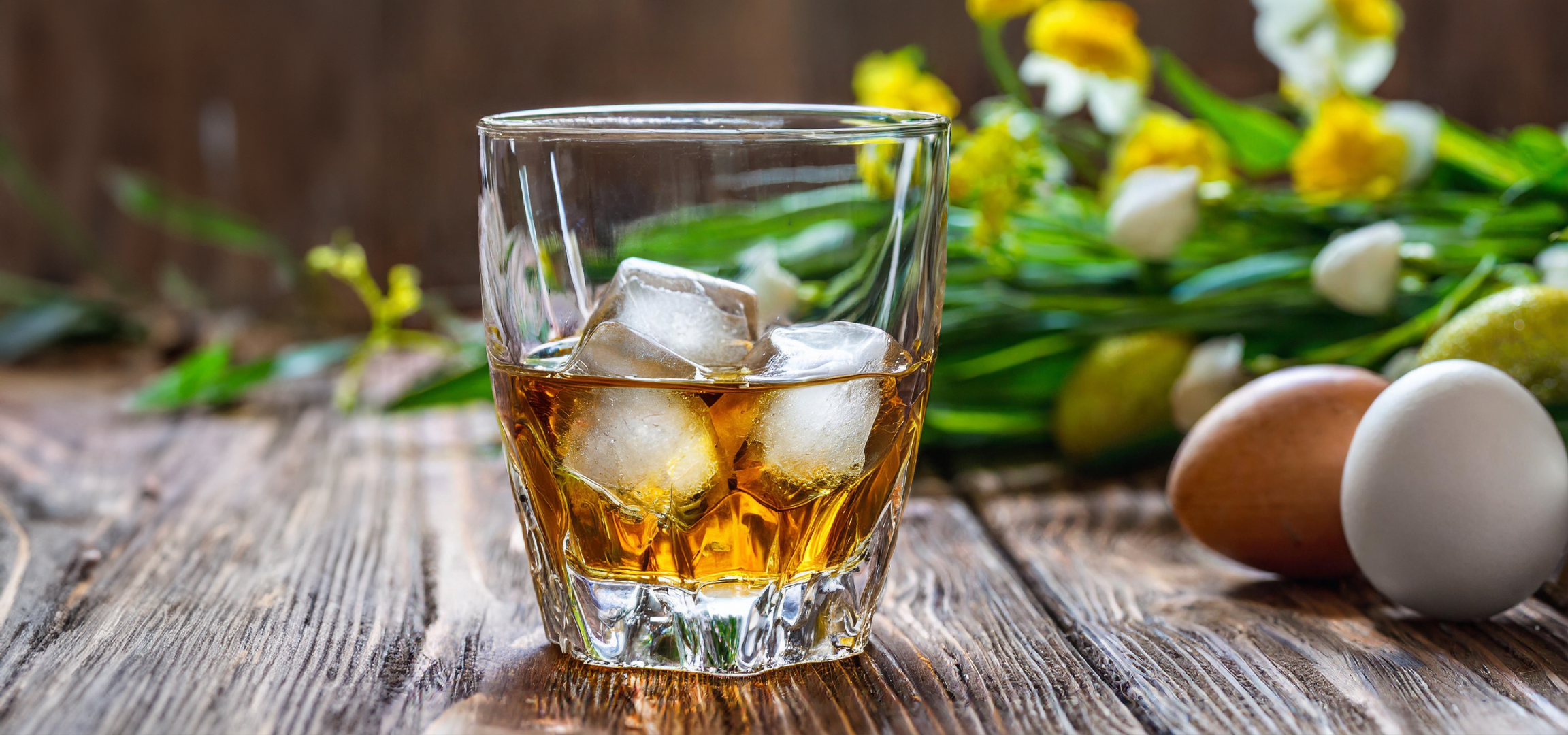 Whisky jéggel, tojások és virágok rusztikus fa asztalon.