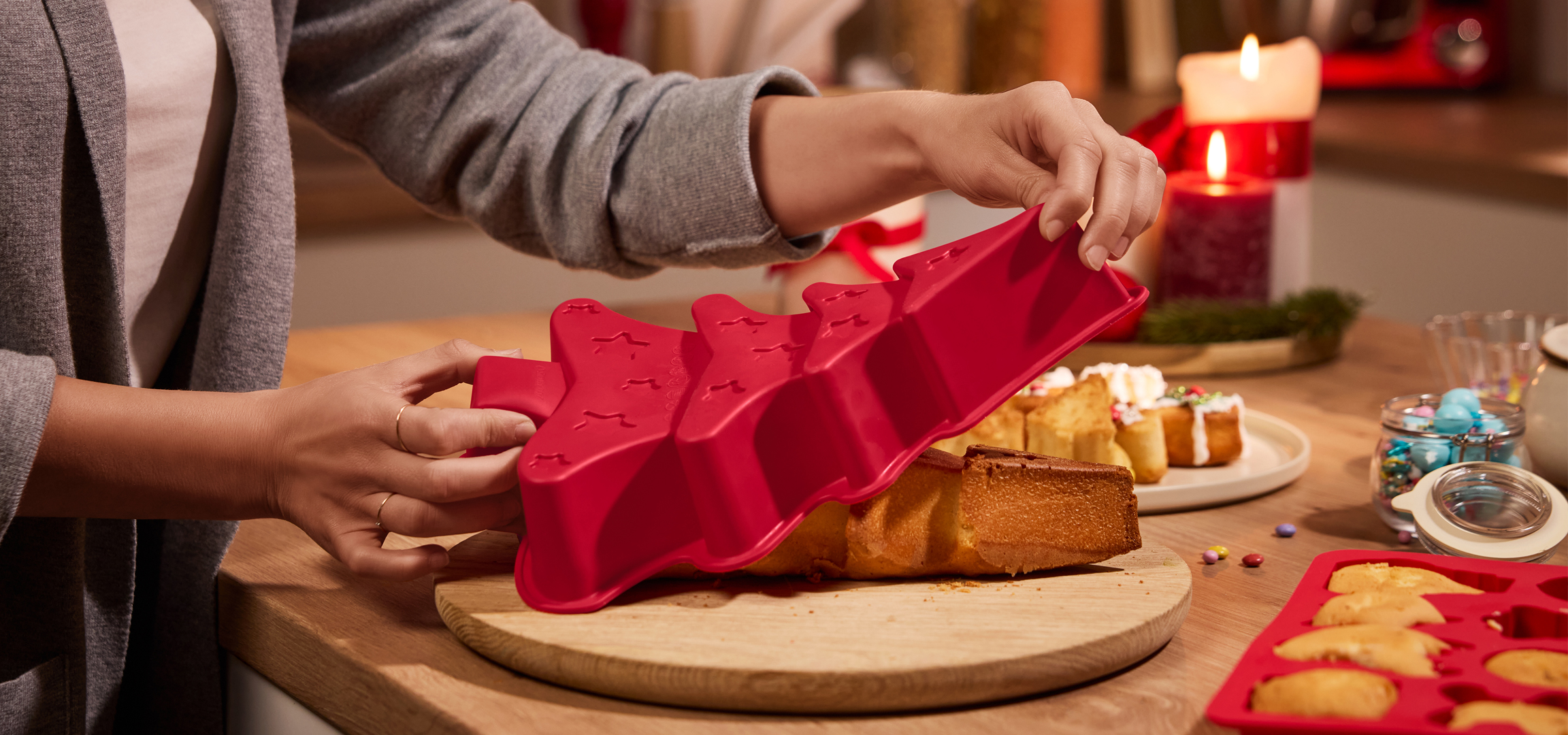 Egy személy kivesz egy karácsonyfa alakú süteményt egy piros szilikon formából.